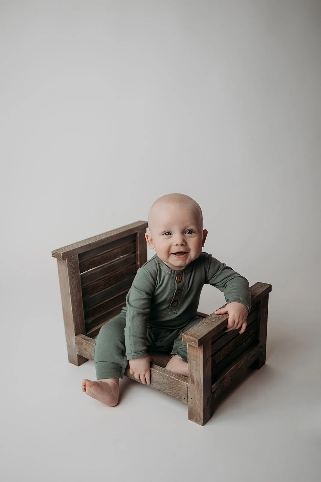 Smiling baby sitting inside a small wooden crate on a plain white background.