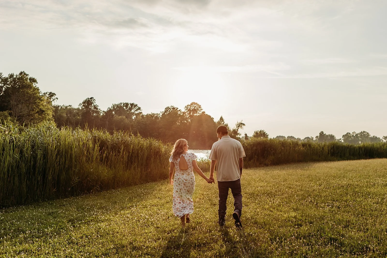 A couple walking hand in hand through a grassy field during sunset.