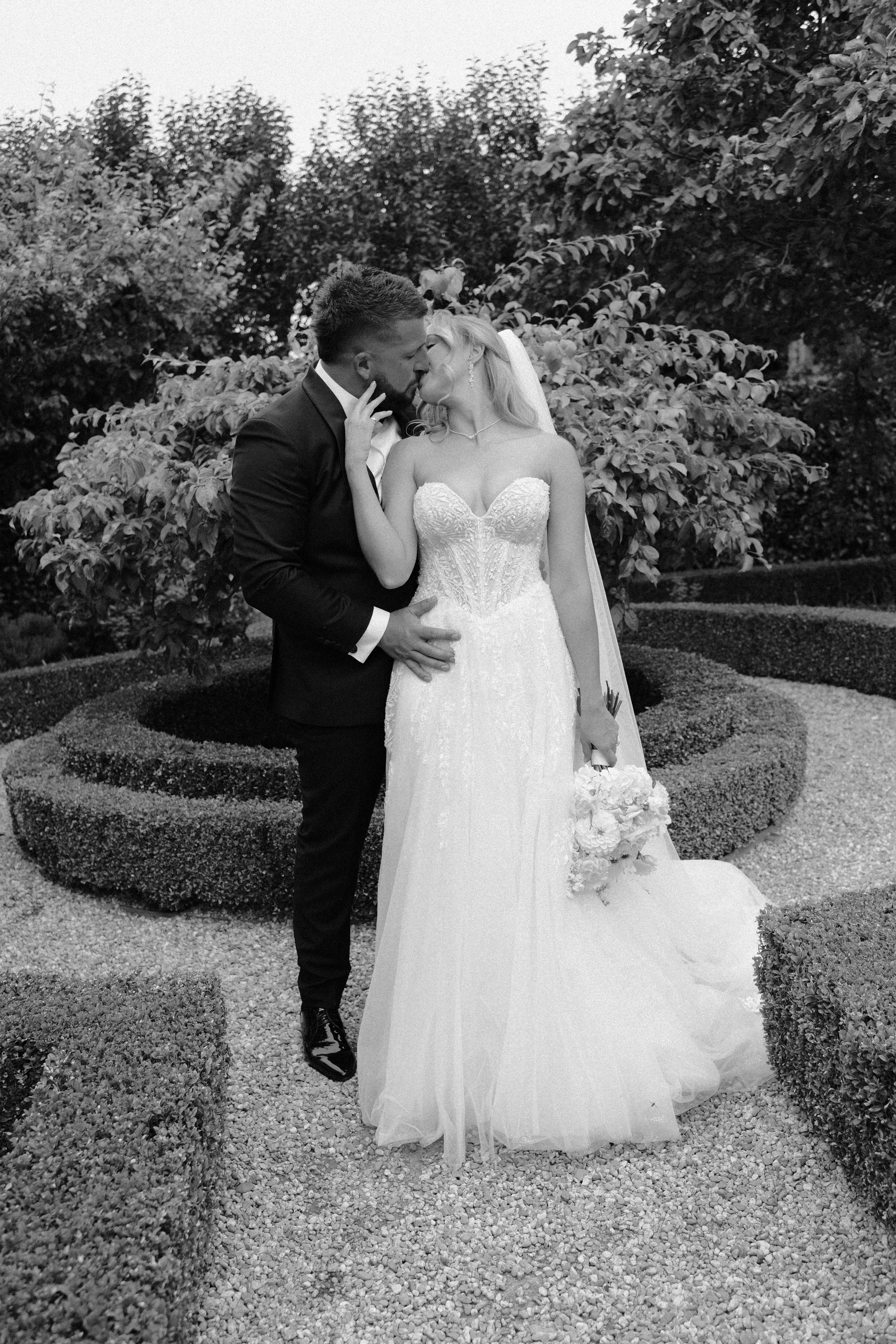 A bride and groom sharing a kiss in a garden, with the bride holding a bouquet of flowers.