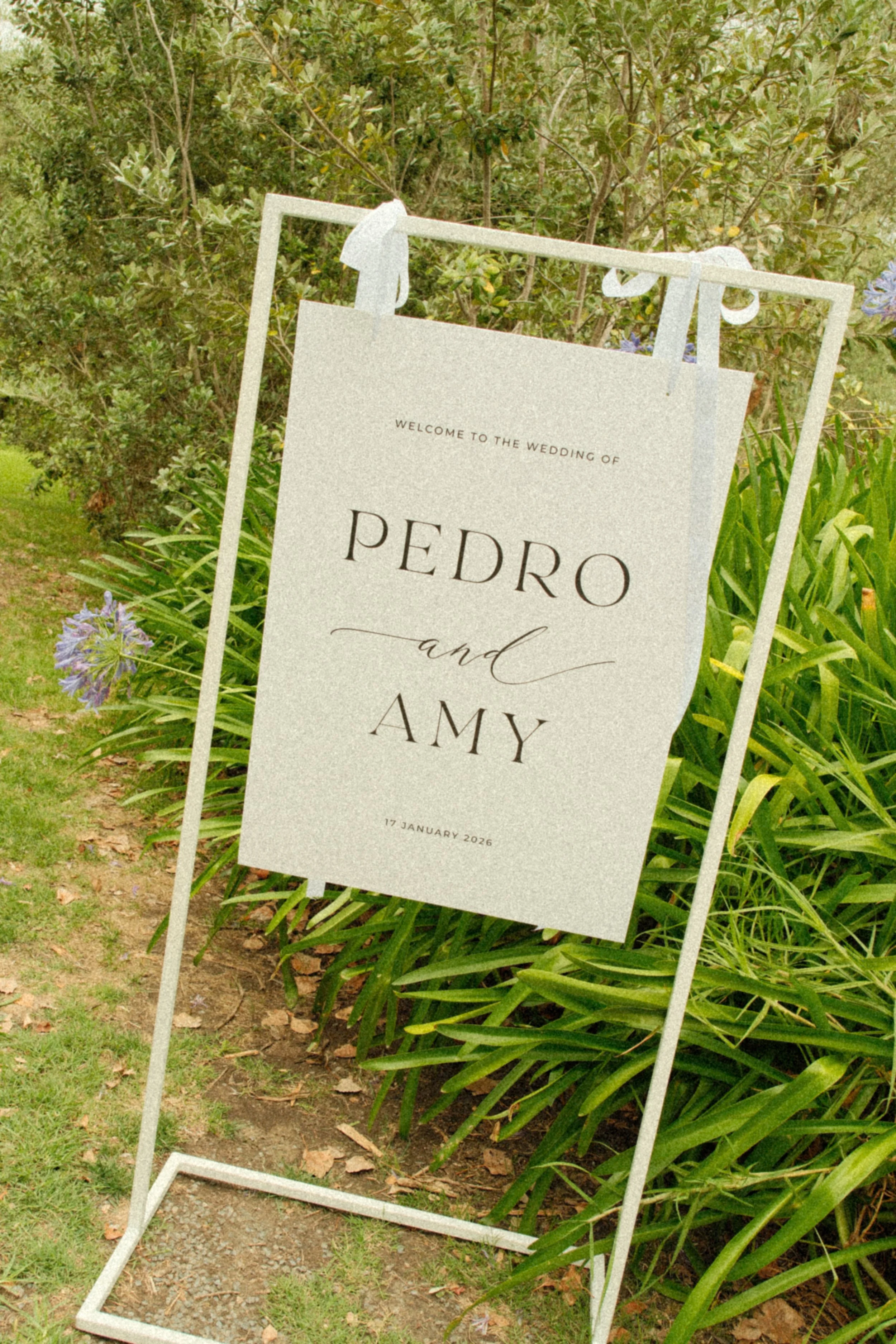 Wedding sign for Pedro and Amy with date January 17, 2026, outdoors among green plants.