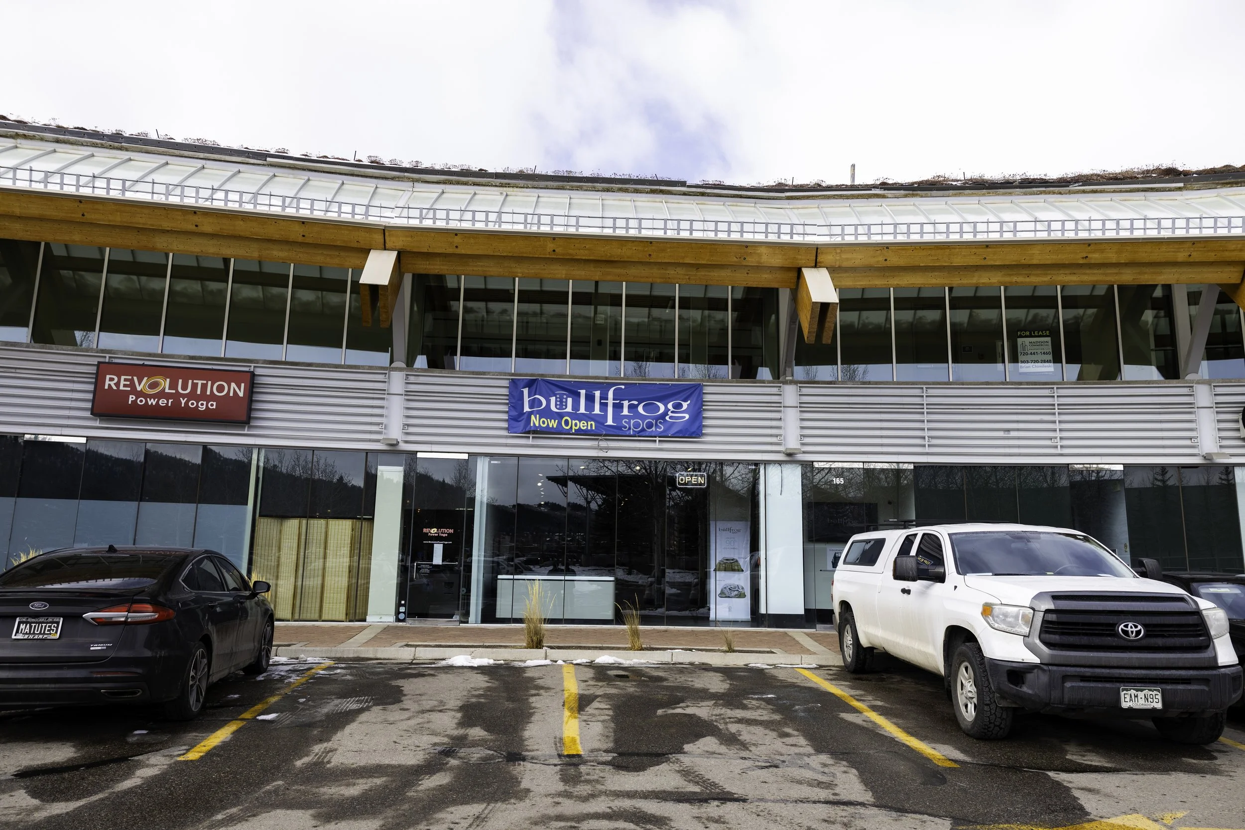 Front view of a commercial building with signs for Bullfrog Spa, parked cars in front, and snow on the ground.