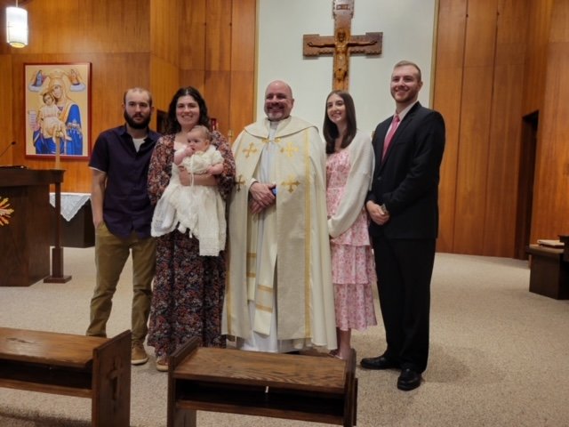 A family standing in a church, with a priest in the center, during a special religious celebration.