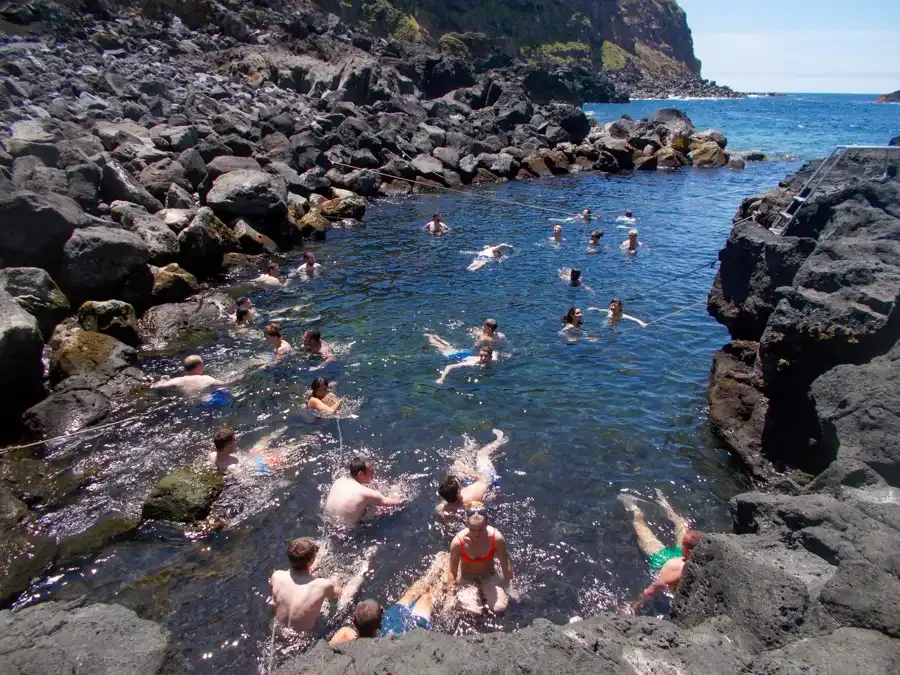 Group of people swimming and relaxing in a rocky coastal cove with cliffs and the ocean in the background.