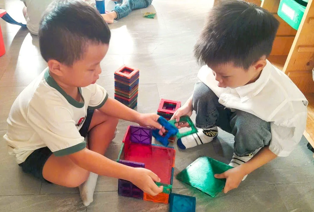 Two boys playing with colorful magnetic building tiles inside a room.
