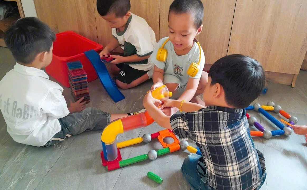 Four young children playing with colorful toy building blocks and pipes on the floor of a room.