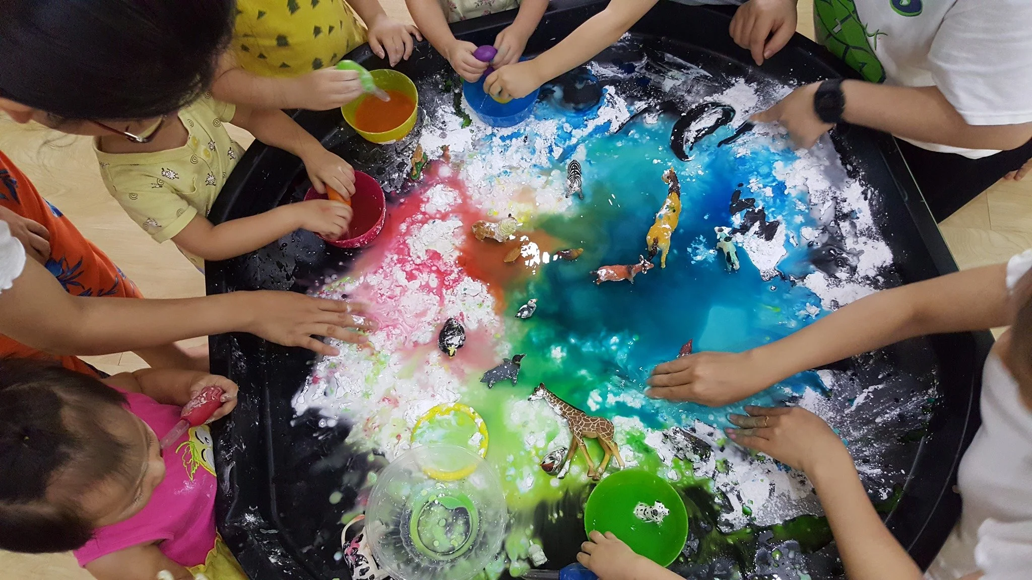 Children playing at an interactive water table with colorful liquids and toy animals.