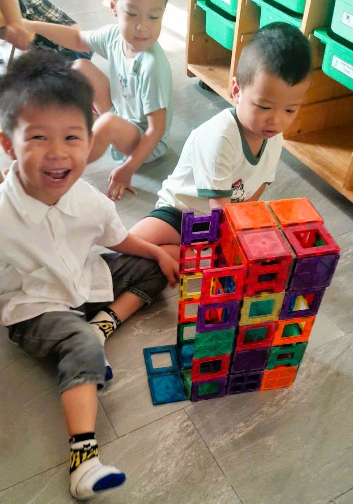 Three children playing with colorful magnetic building blocks in a classroom.