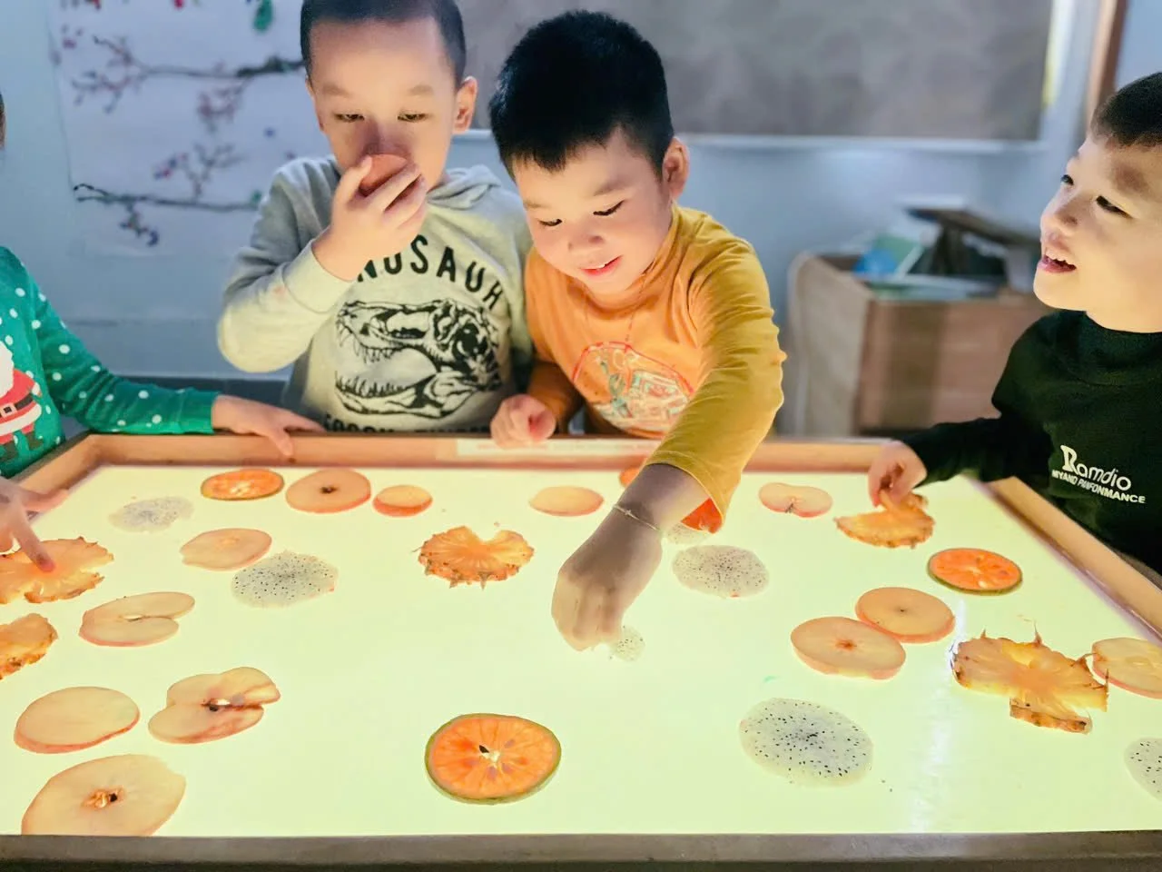 Children experimenting with fake snow and toy penguins in a sensory tray, with a decorated Christmas tree in the background, at Bizzy Bees Preschool & Kids Club.