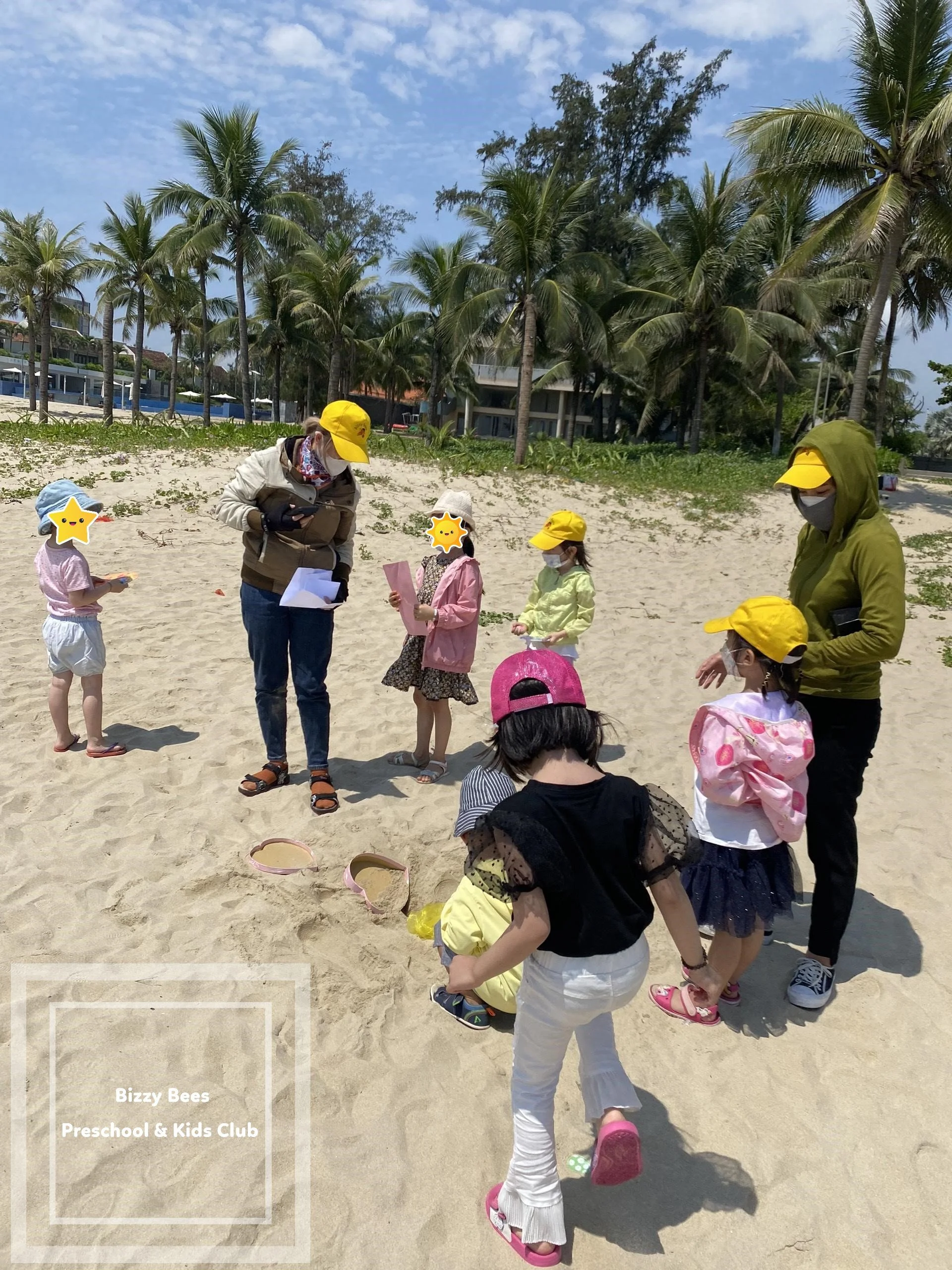 Children and adults on a sandy beach with palm trees in the background, participating in an outdoor activity organized by Bizzy Bees Preschool & Kids Club.