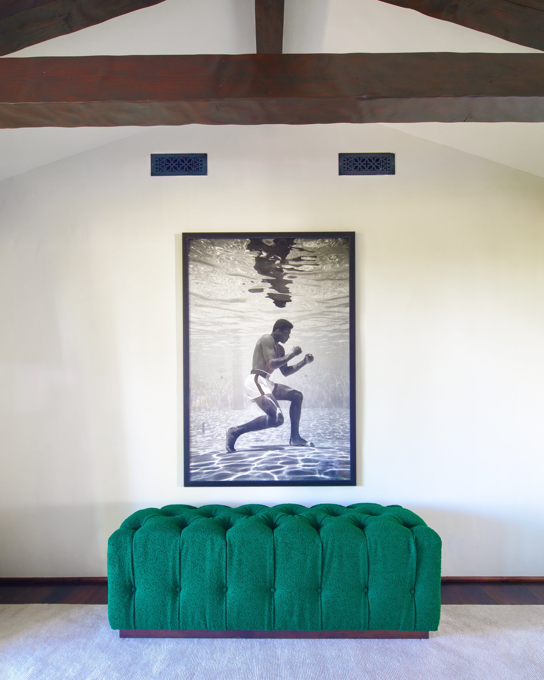 Interior wall with black and white underwater boxing photo above green tufted bench