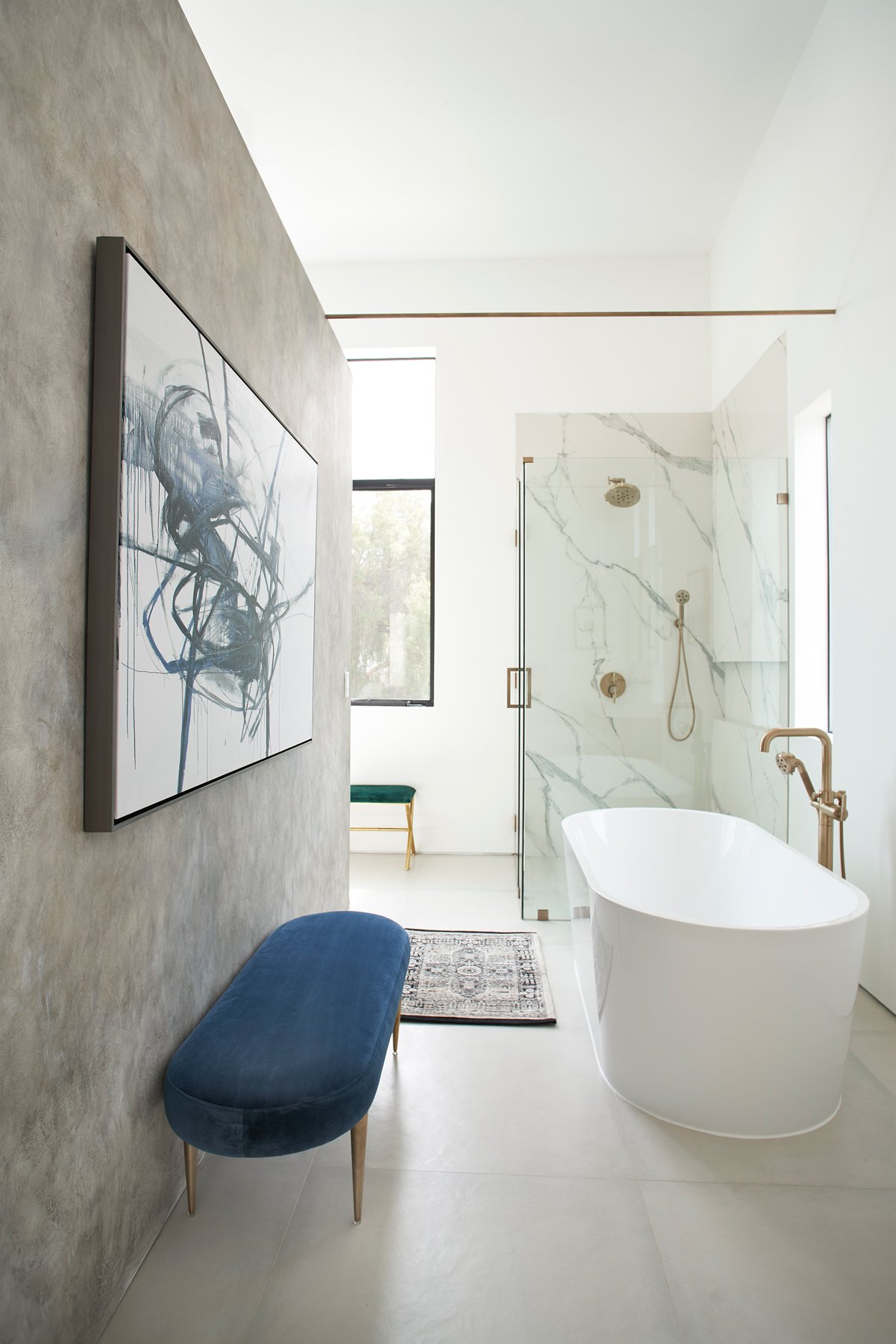 Modern bathroom with freestanding white bathtub, glass-enclosed shower with marble tiles, abstract wall art, and blue bench.