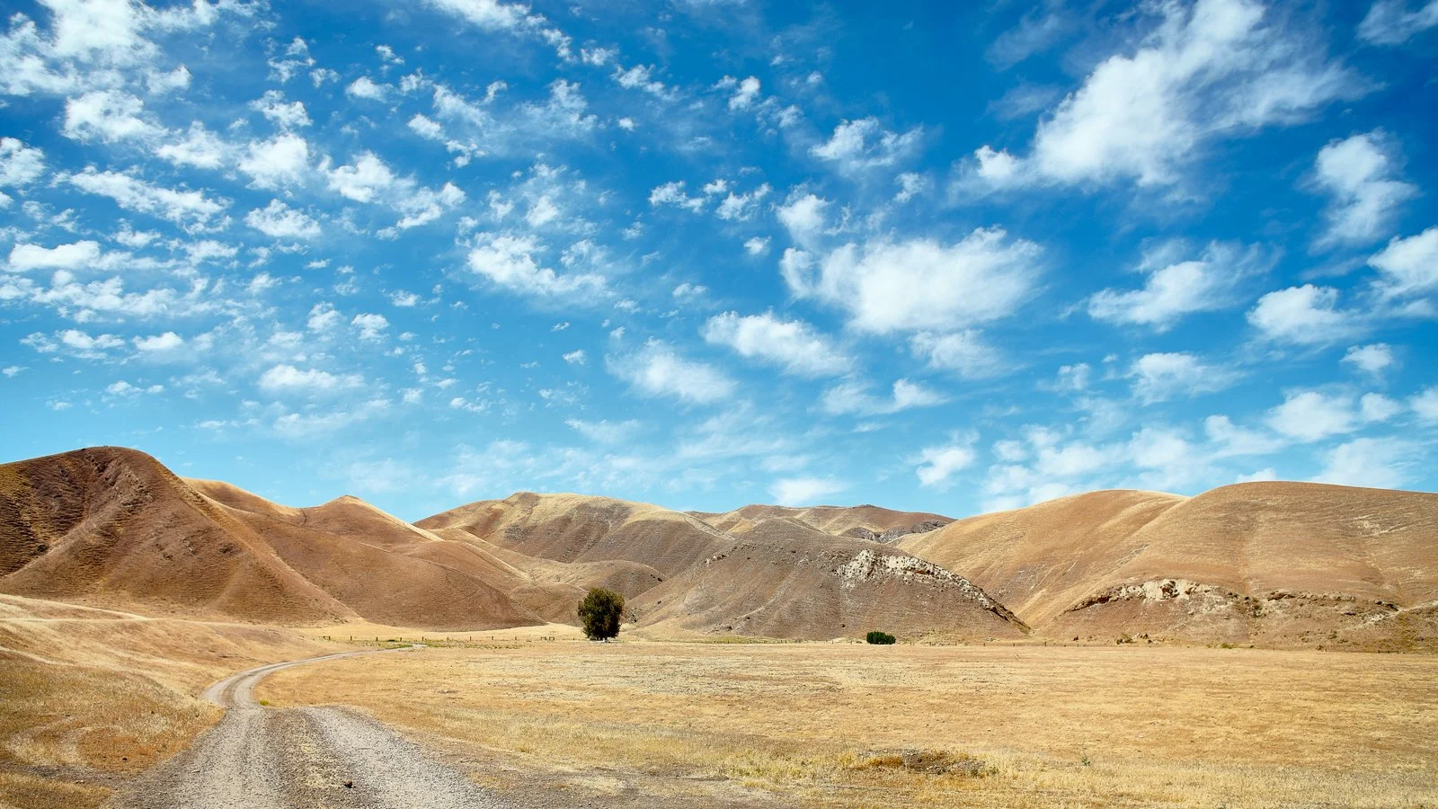 Dry, rolling hills under a blue sky with scattered clouds in a rural landscape.