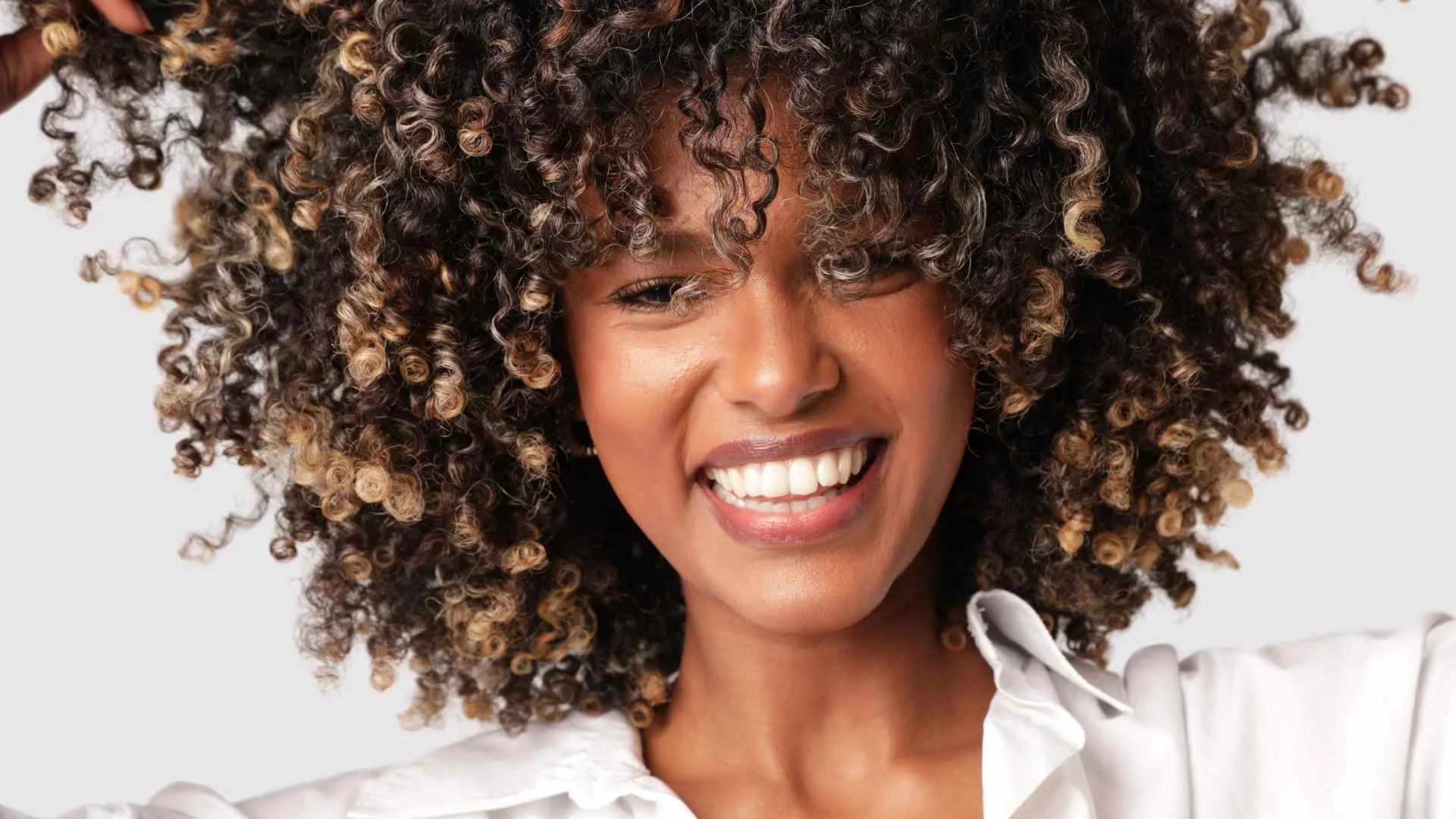 A young woman with curly hair holding a toothpick and looking to the side.