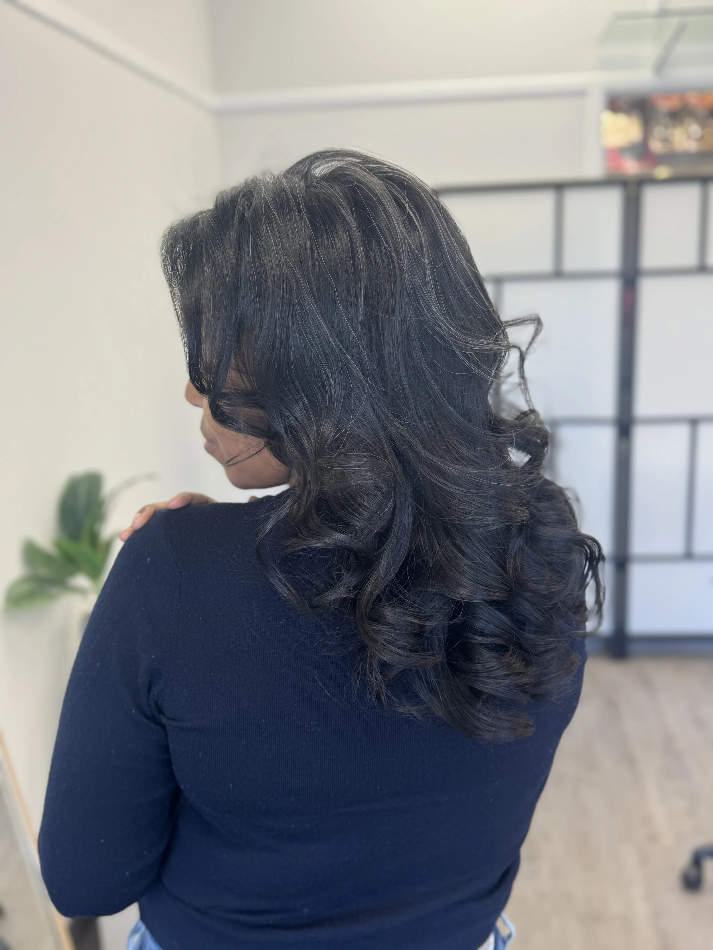 Back view of a woman with shoulder-length black curly hair, wearing a black outfit.