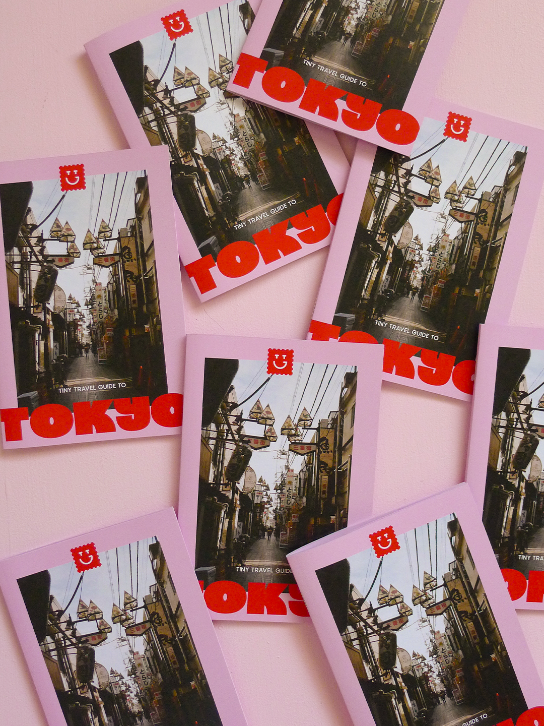 Photo of stacked copies of Tiny Travel Guides to Tokyo. Pink and red cover with a film photo of a Tokyo alleyway.