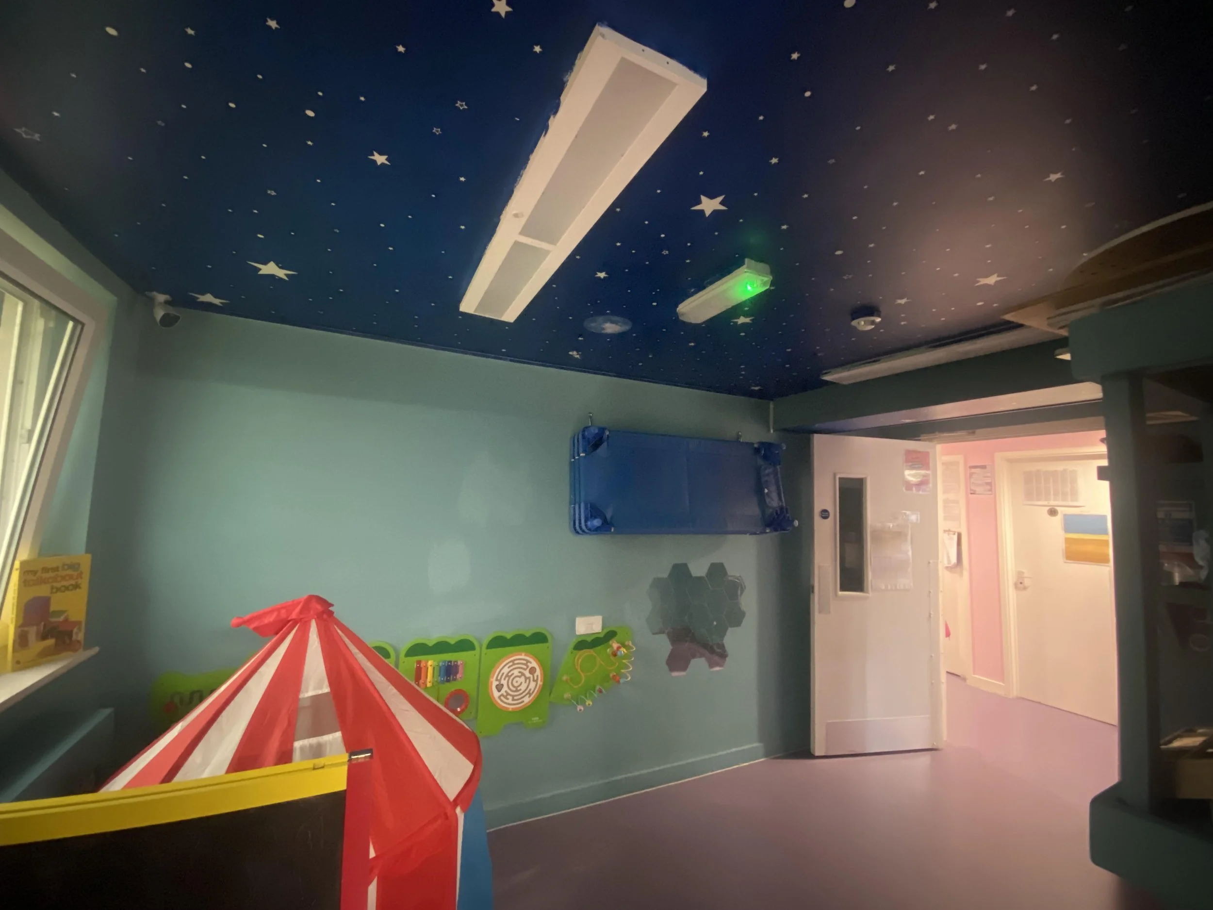 A colorful children's playroom with a starry sky ceiling, green wall accessories, and a red and yellow play tent.