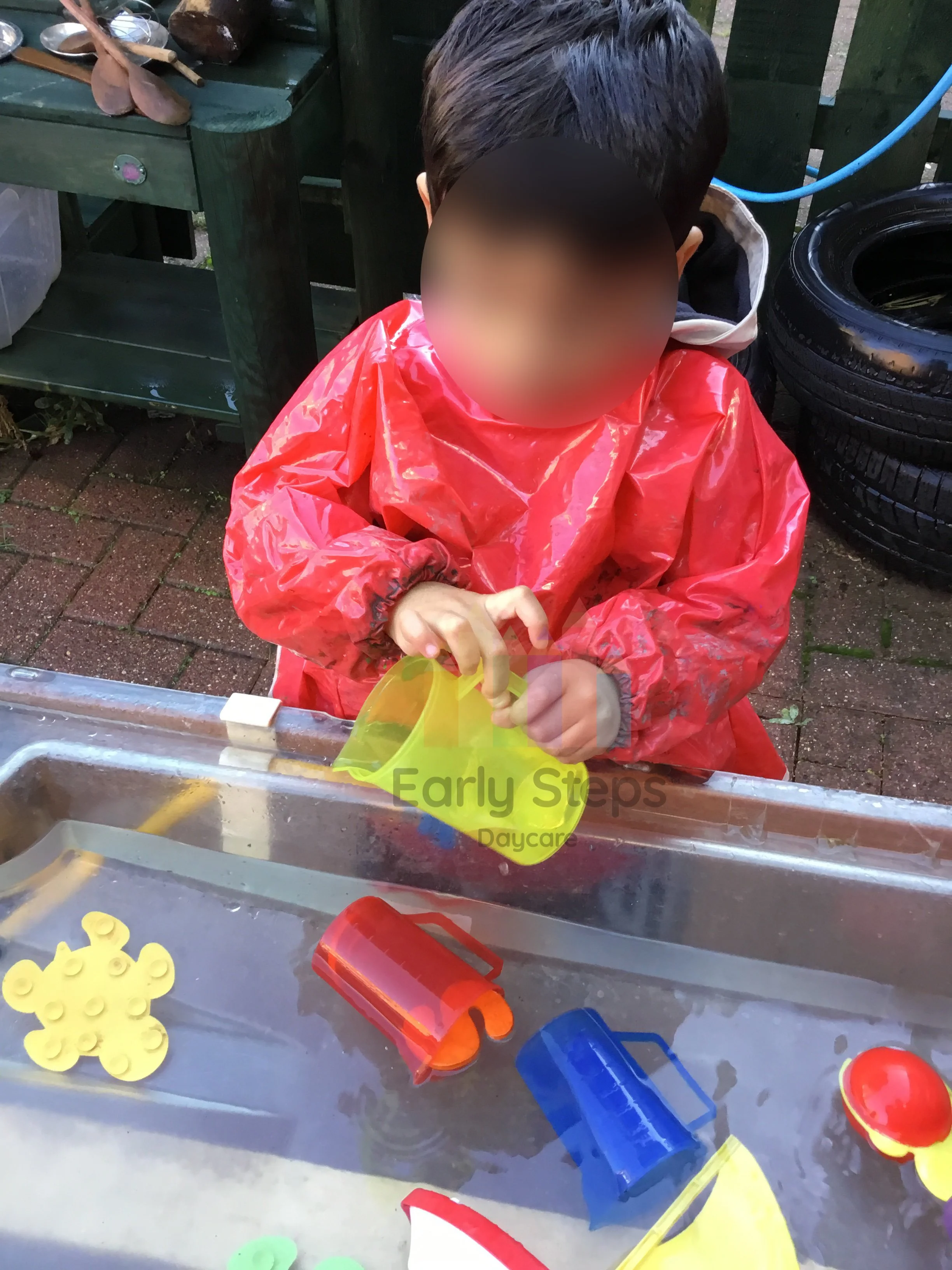 Young child pouring water between jugs during water play at nursery to develop fine motor control and hand-eye coordination.