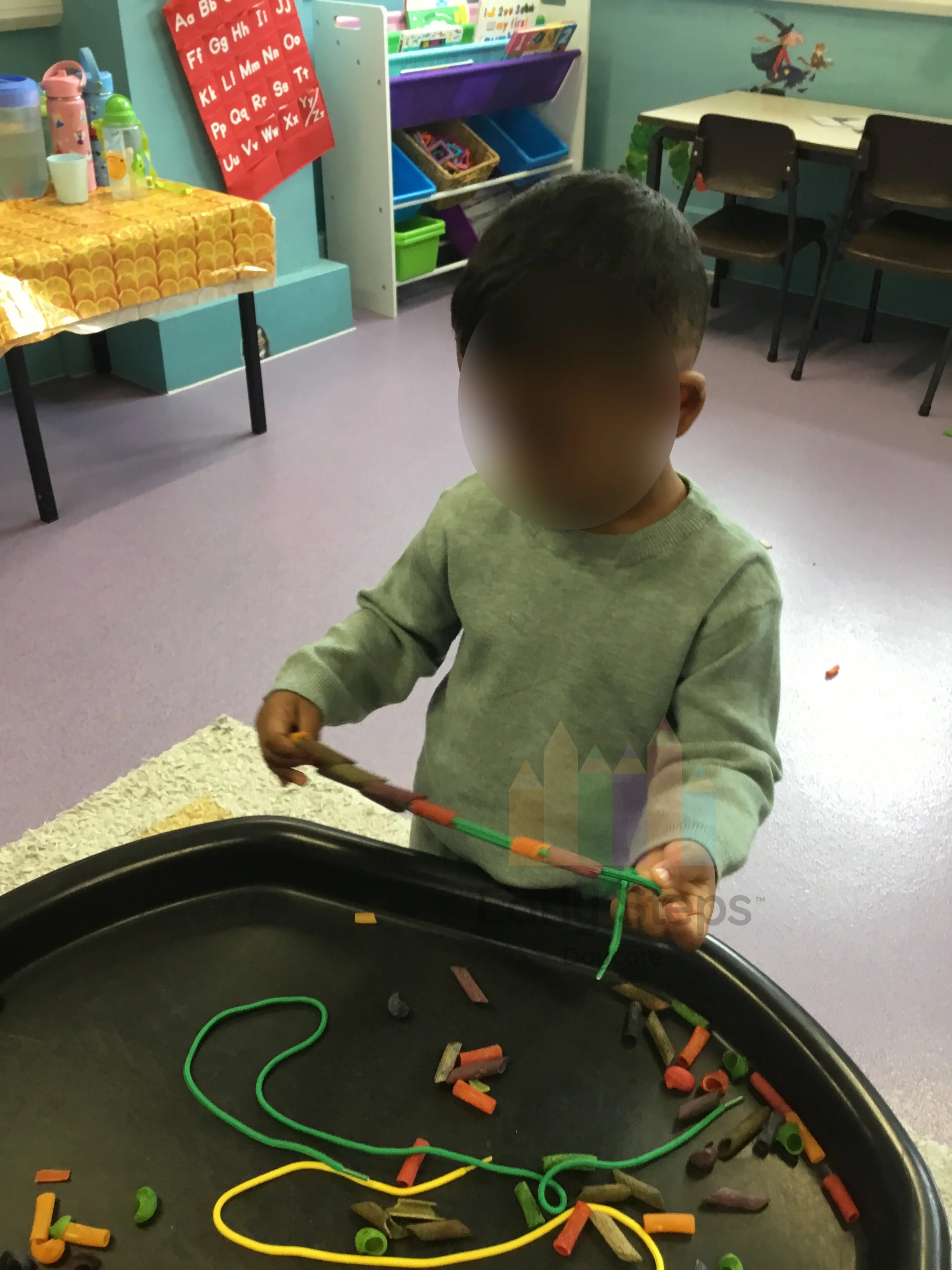 Young child threading coloured pasta onto string in a tuff tray activity to develop fine motor skills and hand-eye coordination.