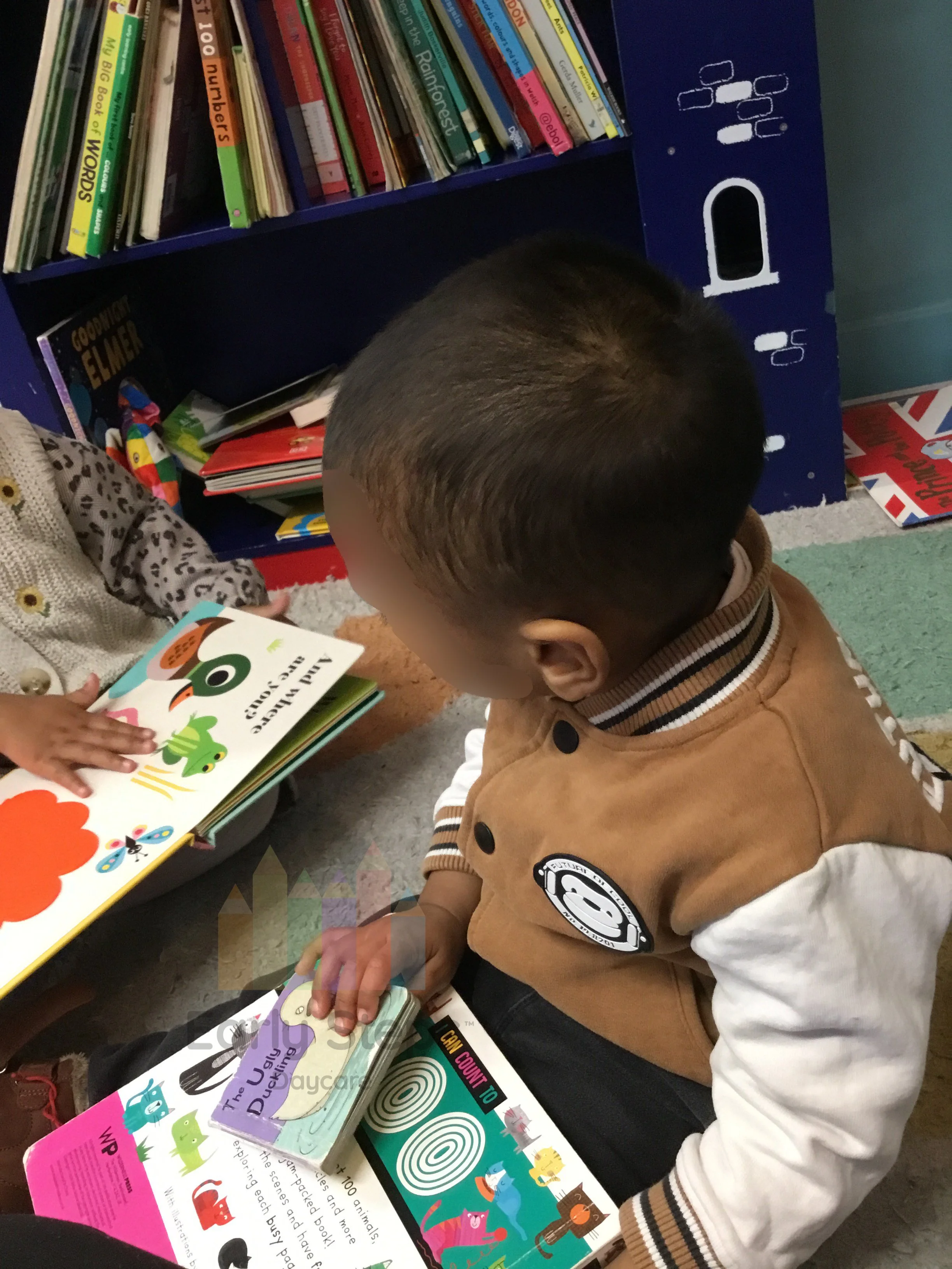 Young child independently looking at a book in the nursery book corner to support communication, language and early literacy development.