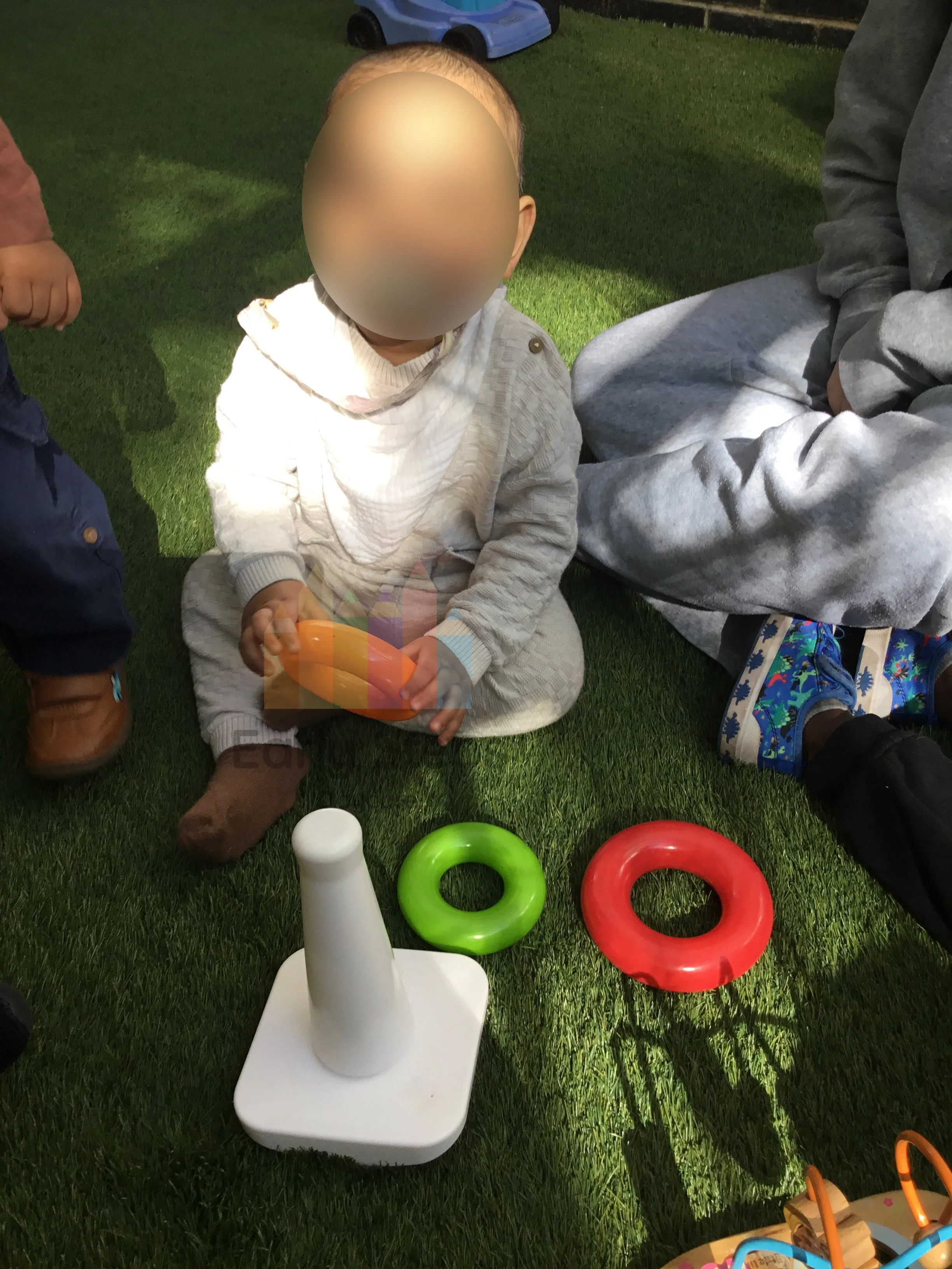 Infant placing different sized rings onto a stacking pole toy at nursery to support fine motor skills and hand-eye coordination.