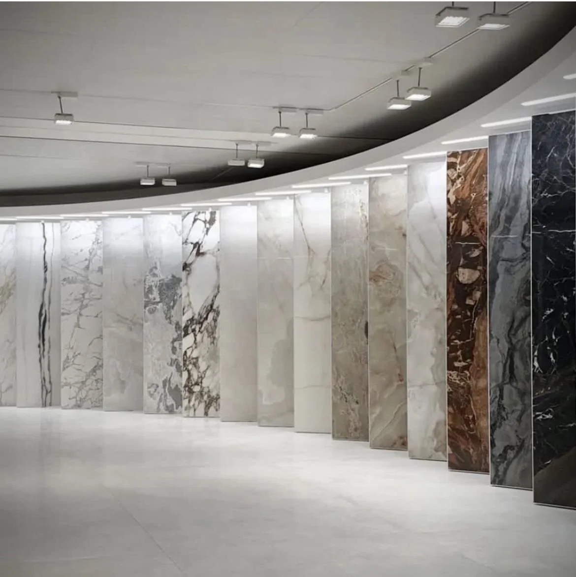 Mostra di pannelli di marmo di diversi colori e motivi in una galleria luminosa con soffitto a pannelli e luci