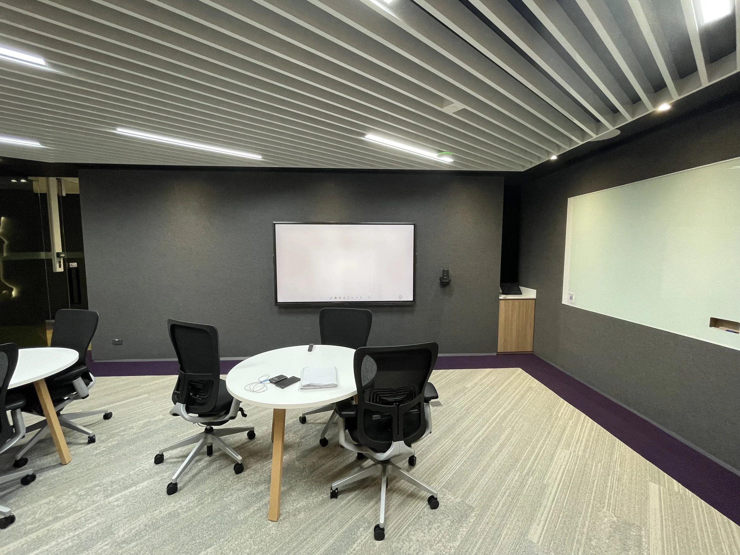 Small collaboration meeting room on a BPO production floor in Thailand featuring a round table, task chairs, and integrated audiovisual display