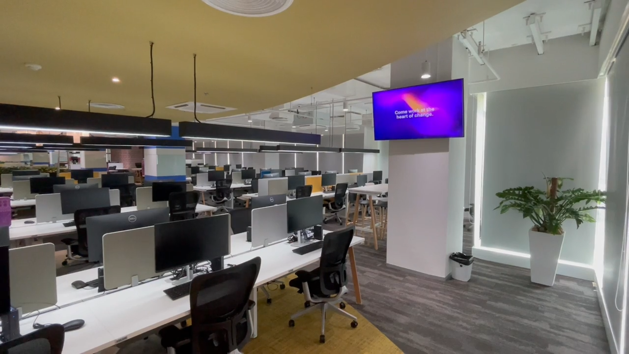 Open plan BPO production floor in Thailand with rows of workstations, integrated audiovisual displays and collaborative work areas.