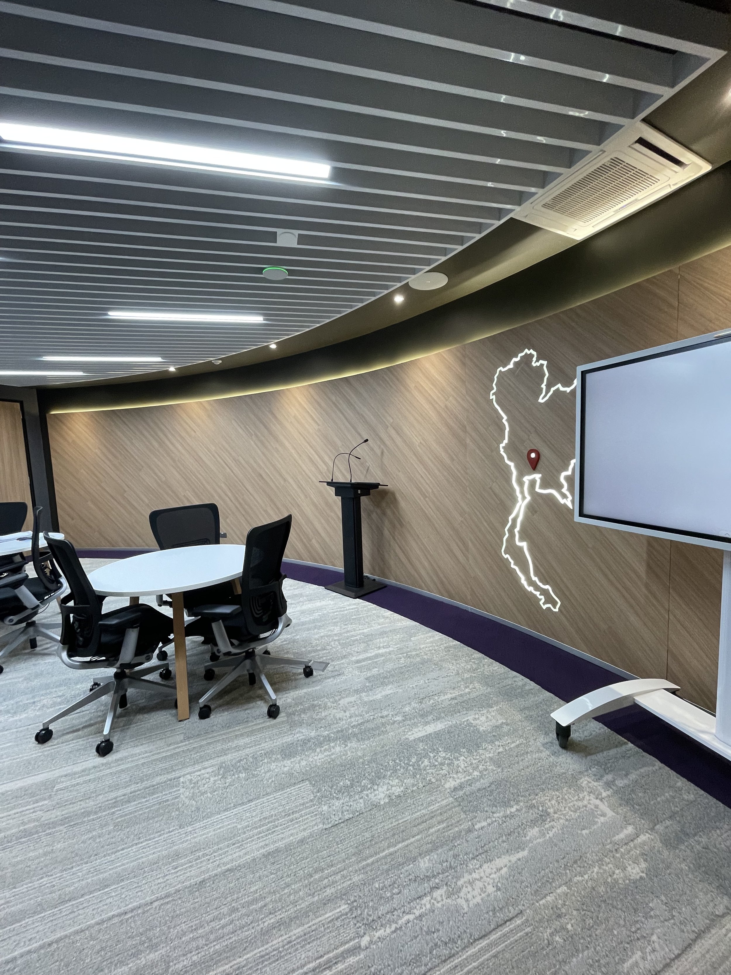 Collaborative meeting area on a BPO production floor in Thailand with curved feature wall, integrated display, and presentation lectern
