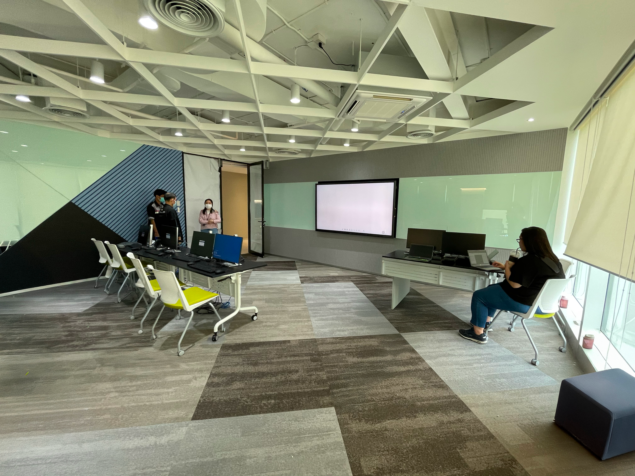 Flexible training and collaboration space within a BPO production floor in Thailand with modular tables, displays, and team members using audiovisual technology