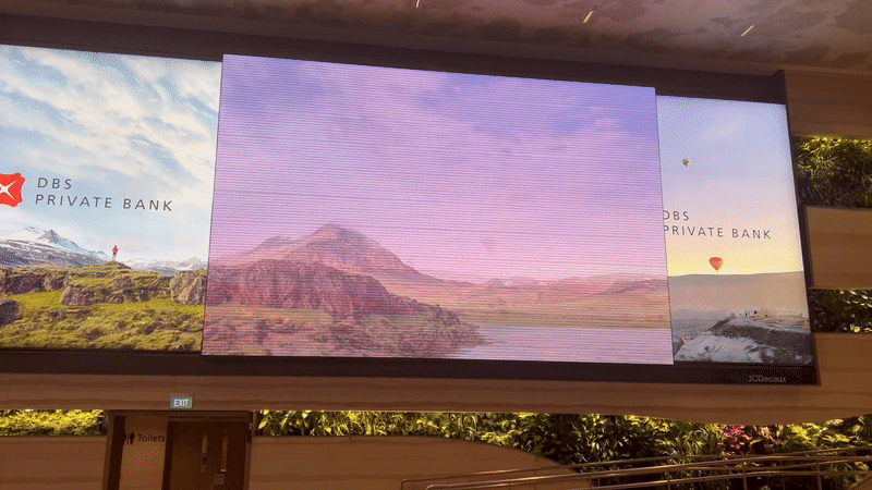 Large digital slider display showing branded content on an LED screen within an airport terminal.