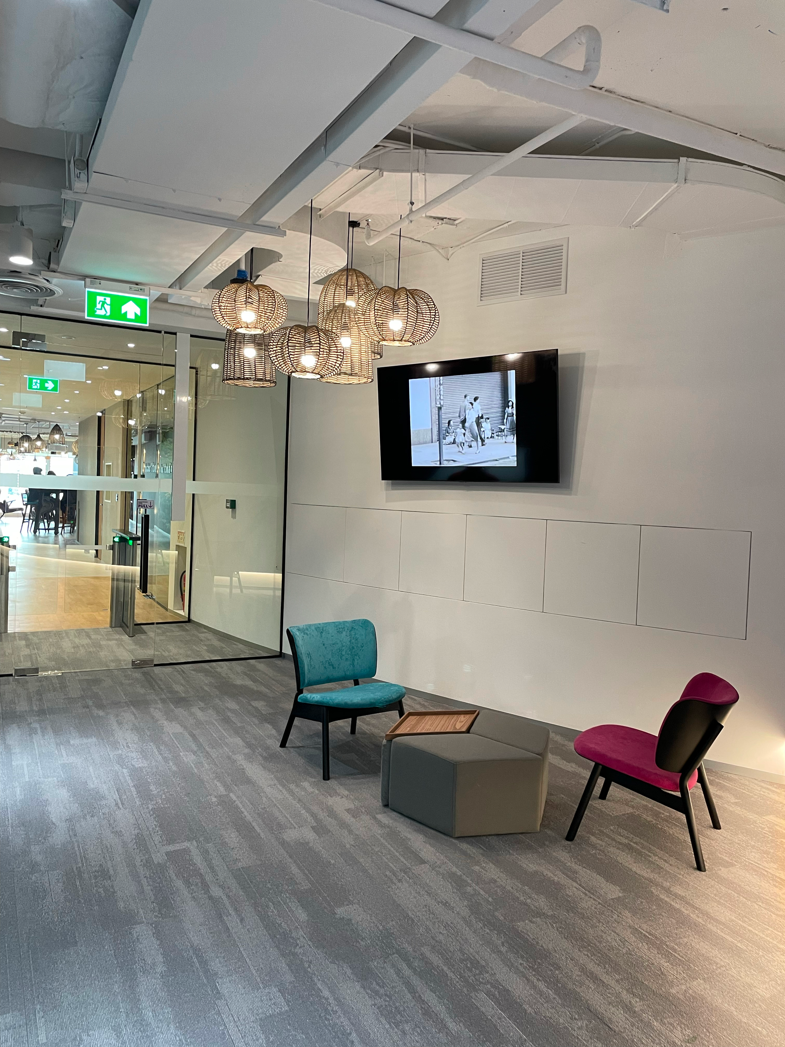 Breakout and waiting area in a Thailand BPO office featuring lounge seating, decorative lighting and a wall mounted digital display.