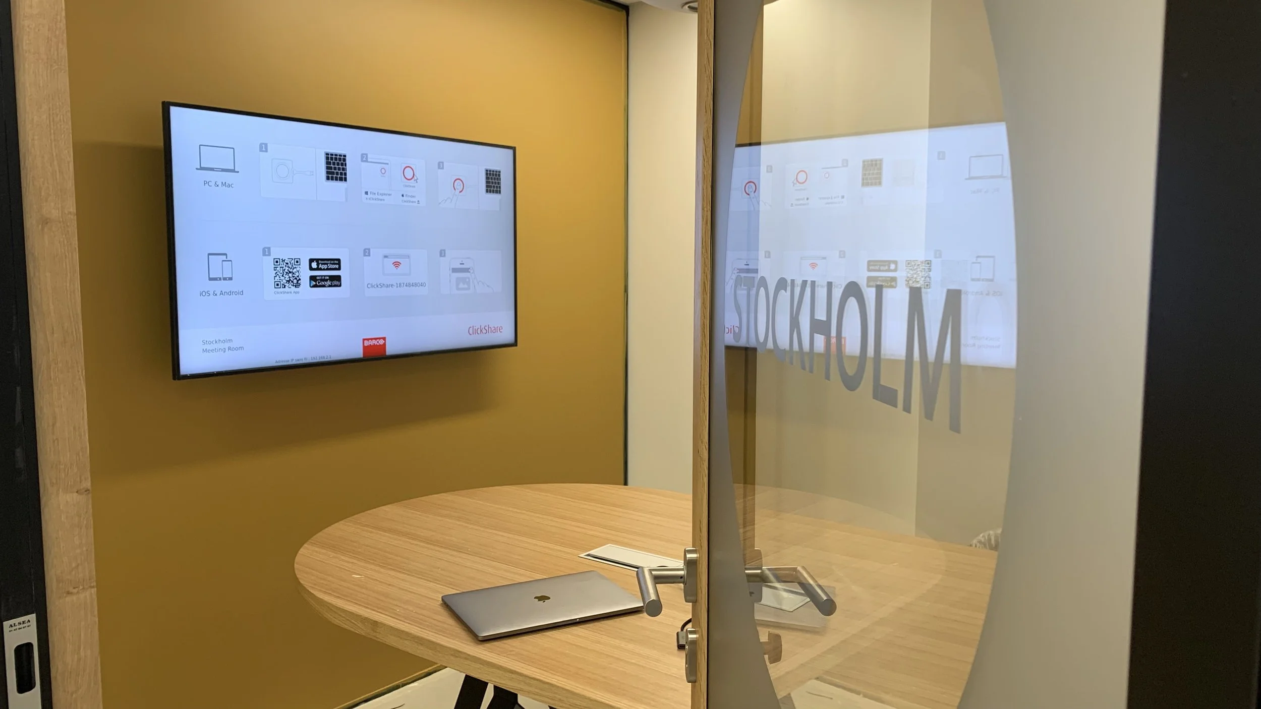Small collaboration room featuring wall mounted display and video conferencing technology for hybrid meetings