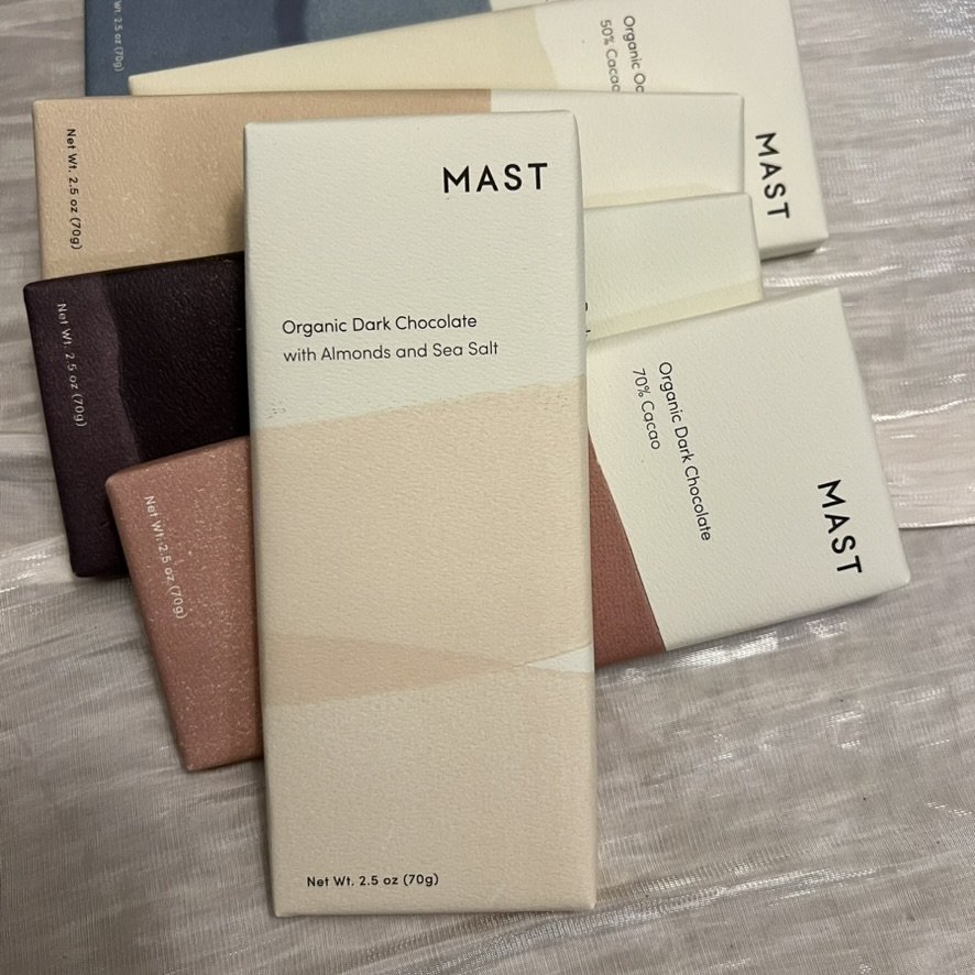 Assortment of Mast gluten-free, dairy-free organic dark chocolate bars in minimalist packaging, featuring flavors like Almonds and Sea Salt.