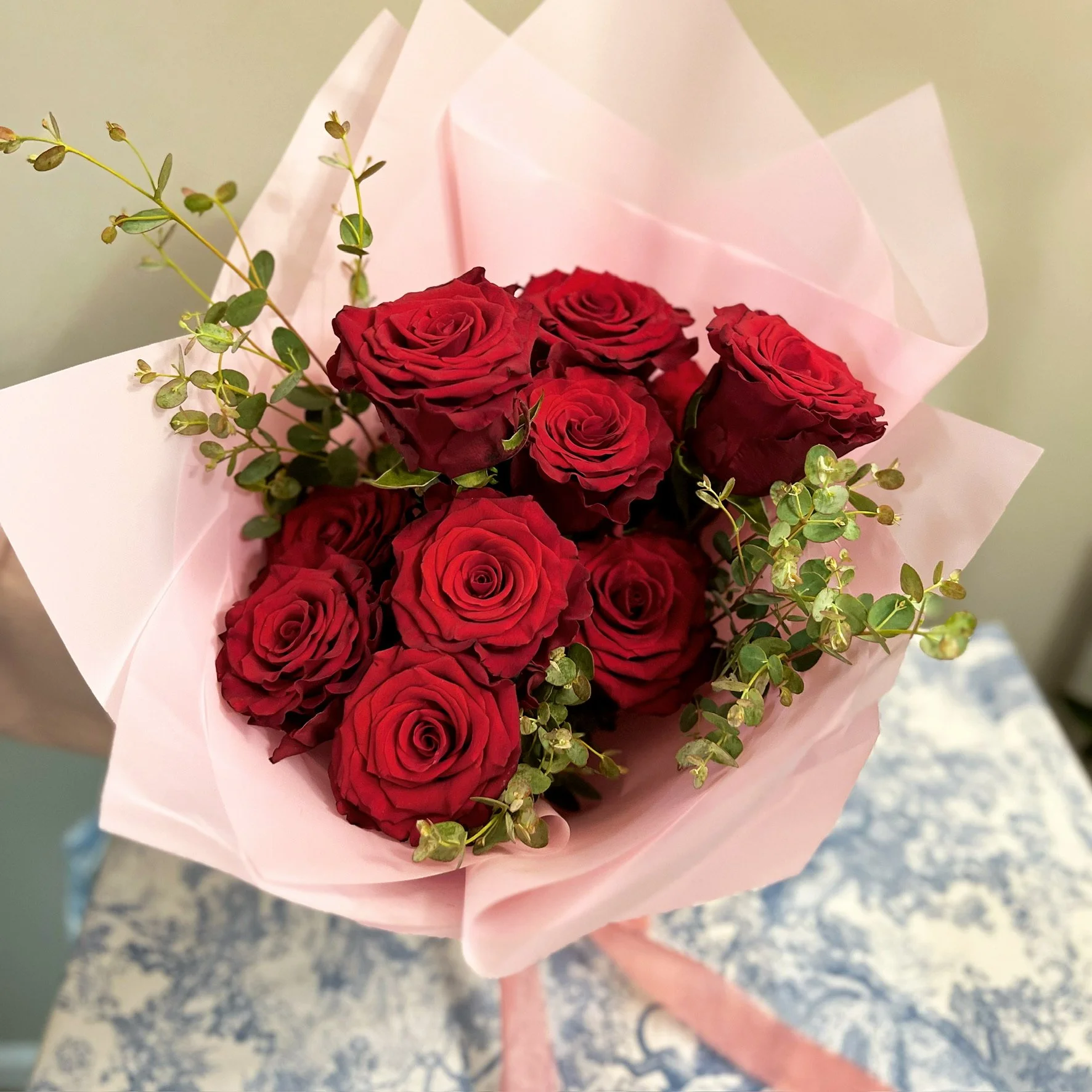 Vibrant dozen red rose bouquet with mixed greenery, artistically wrapped in variable colored paper, by Meadow Edge Blooms flower studio