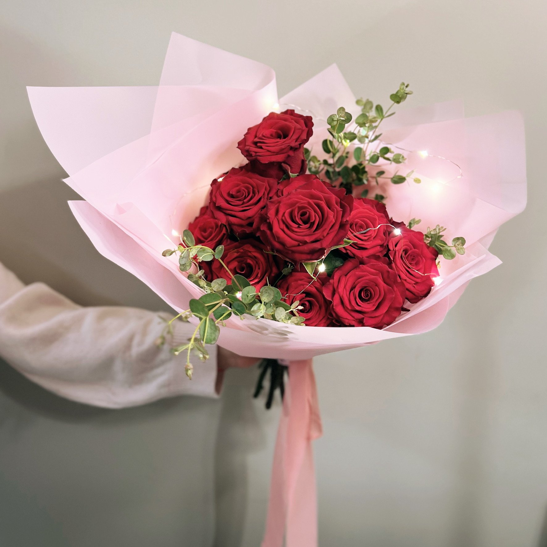 Vibrant dozen red rose bouquet with mixed greenery, artistically wrapped in variable colored paper, by Meadow Edge Blooms flower studio.