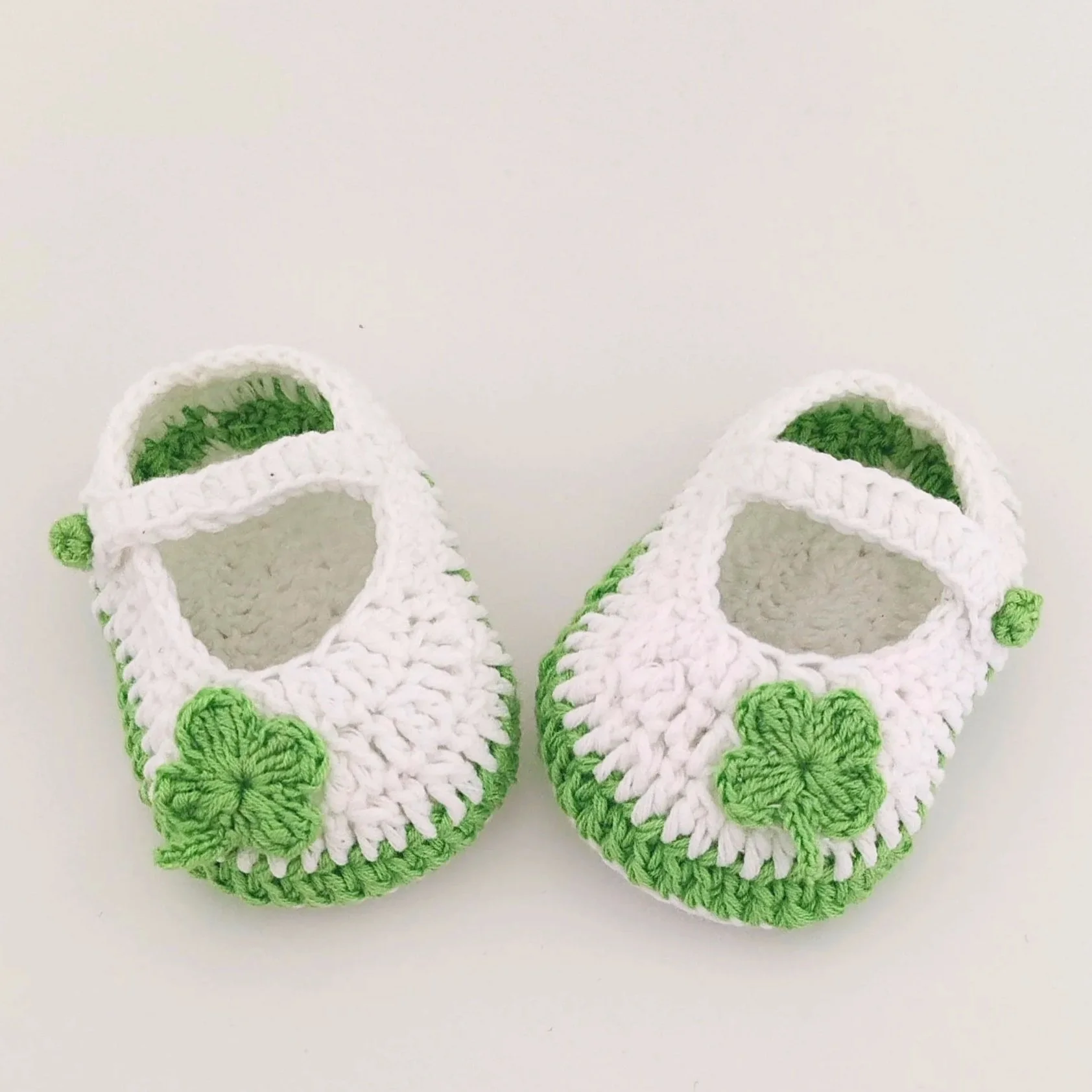 Hand-crocheted white Mary Jane newborn baby shoes with small lucky clover flower appliques