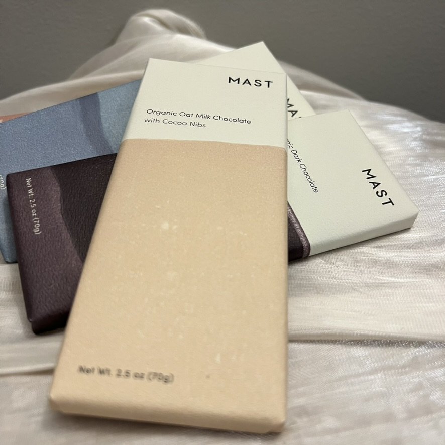 Assortment of Mast gluten-free, dairy-free organic dark chocolate bars in minimalist packaging, featuring flavors like Oatmilk with cocoa nibs.