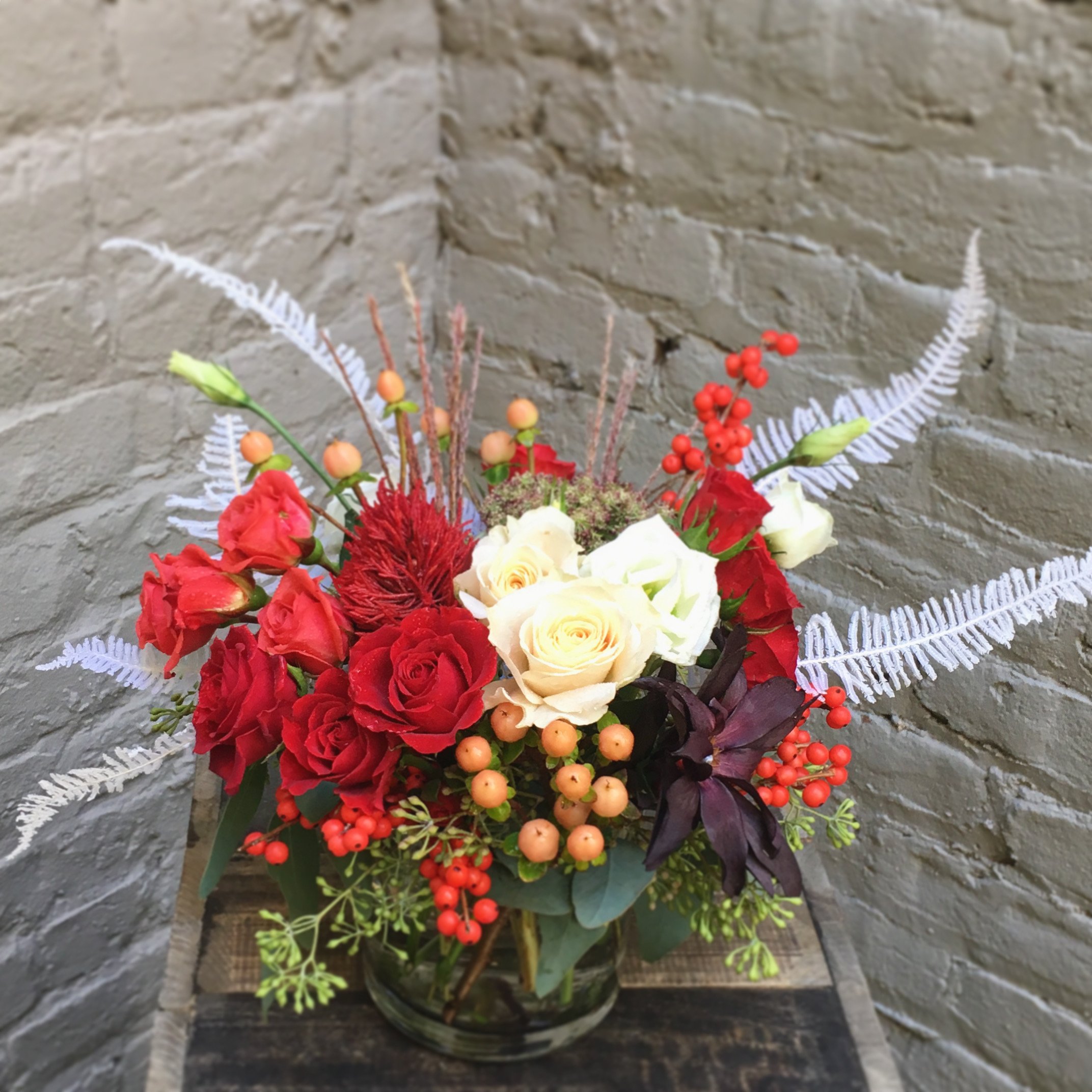 A luxurious Christmas floral arrangement featuring red roses, soft cream and blush blooms, festive red berries, Holiday greenery, perfect for holiday décor or gifting.