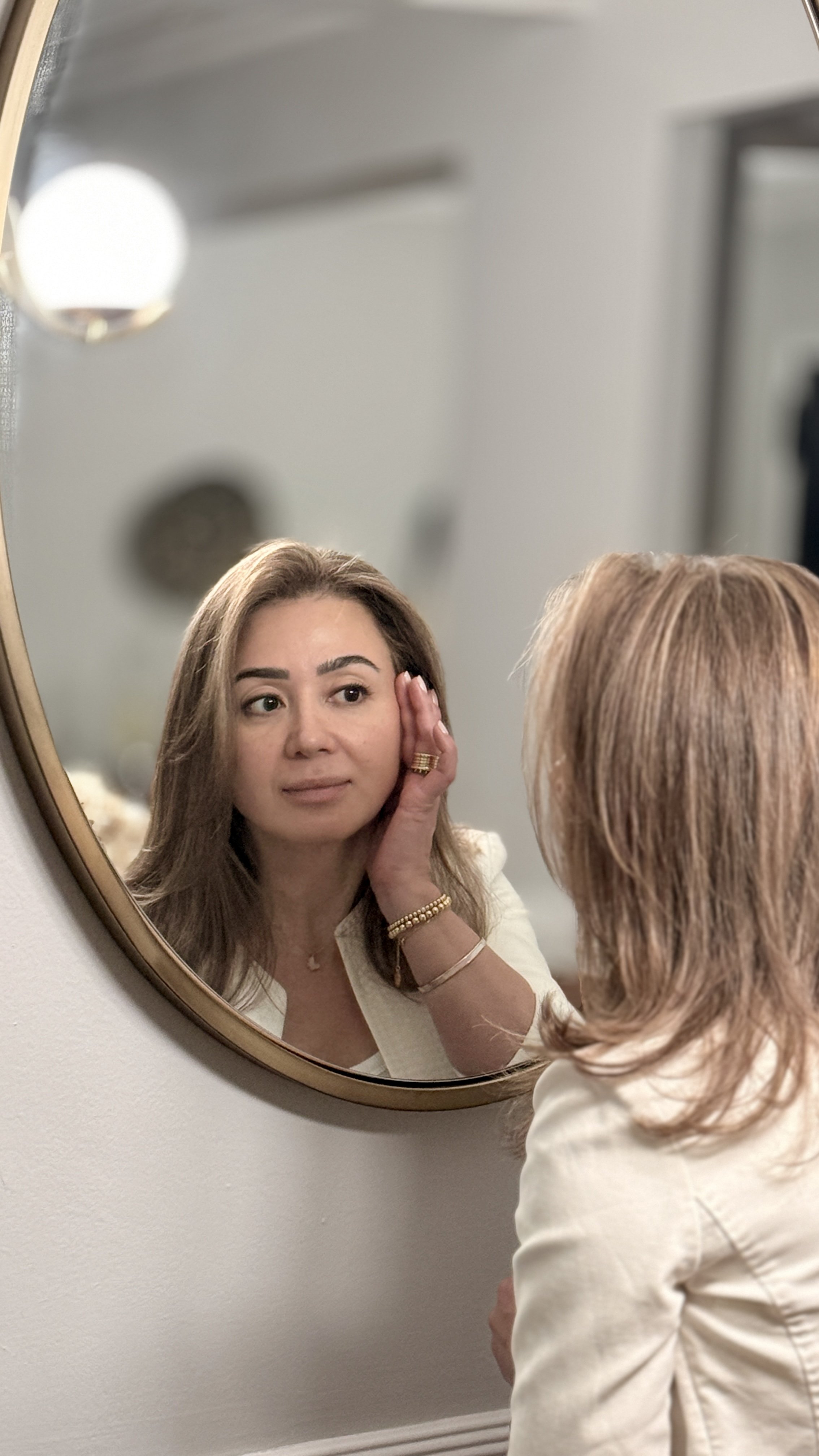 Woman in her 50s looking in mirror confident in her anti-aging skincare routine