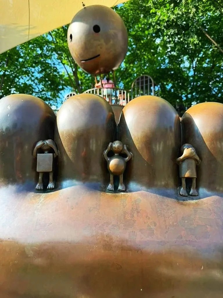 Small sculpted figures hidden between the oversized bronze toes of a playground sculpture, encouraging children to discover playful details.