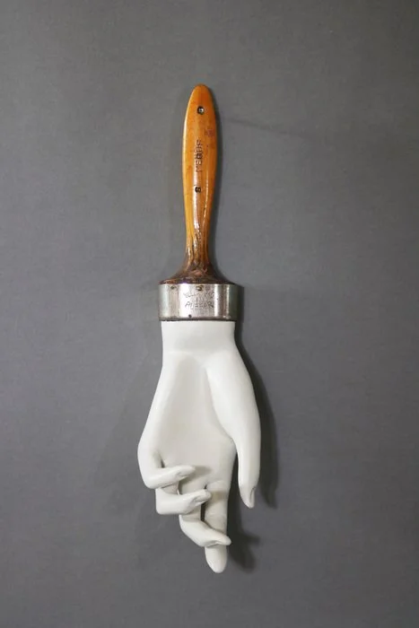 A paintbrush with a hand-shaped brush head attached to the handle, resembling a hand with fingers.