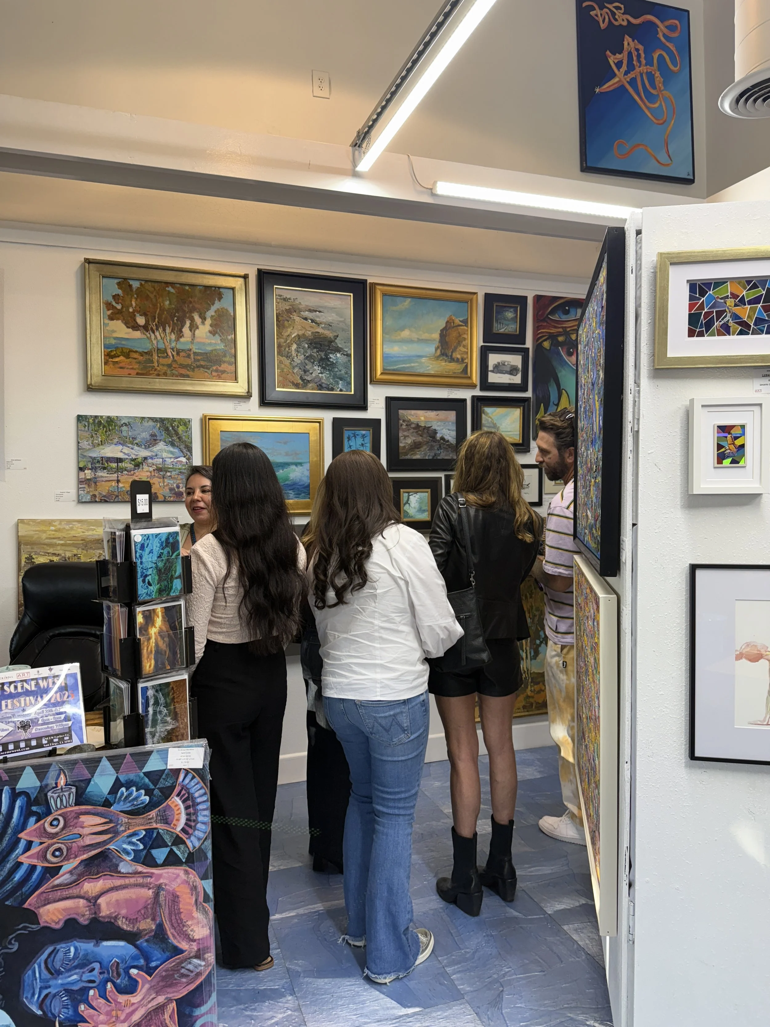 Group of four people at an art gallery viewing various paintings on the wall and standing near display racks.