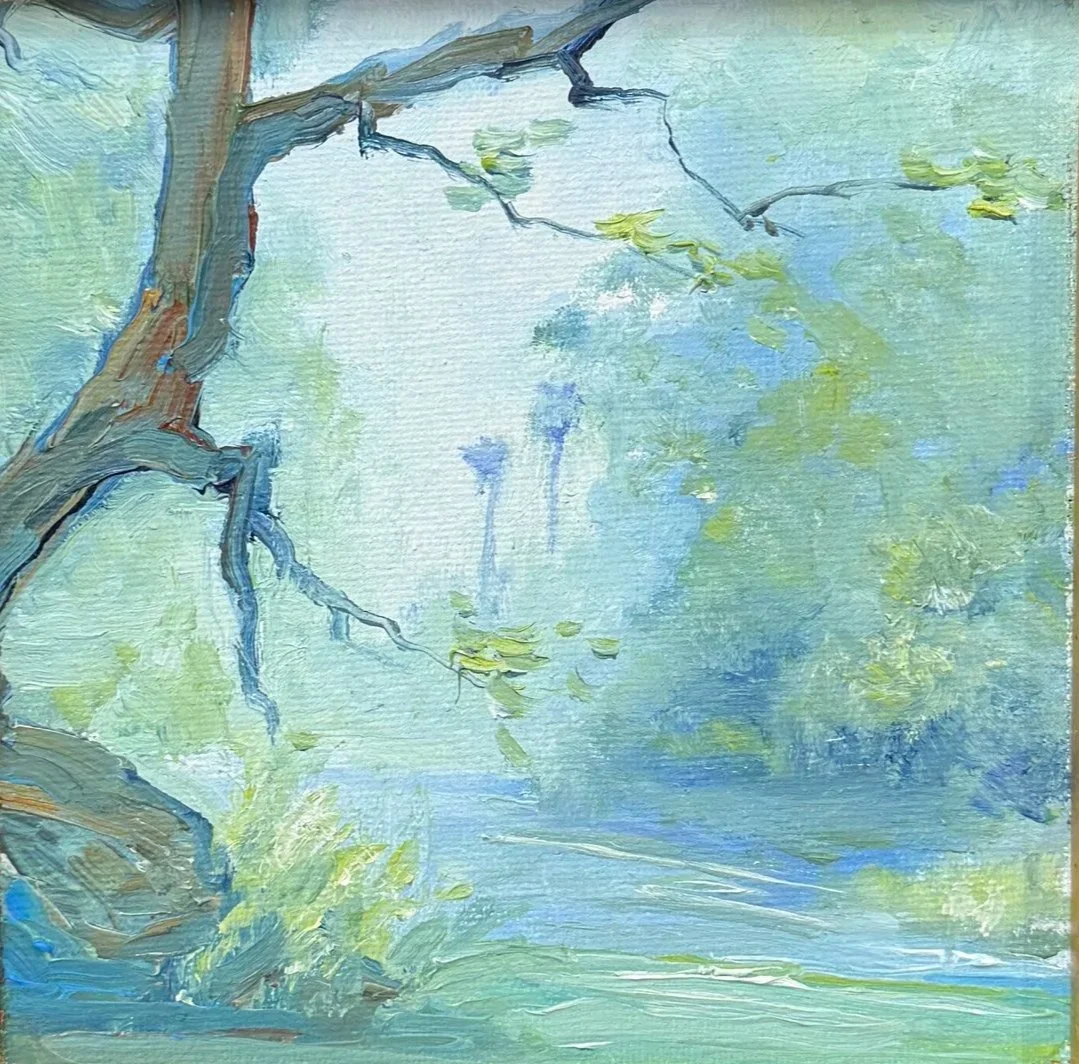 Close-up of a framed landscape painting of a tree with blue sky and green foliage, hanging on a white wall.