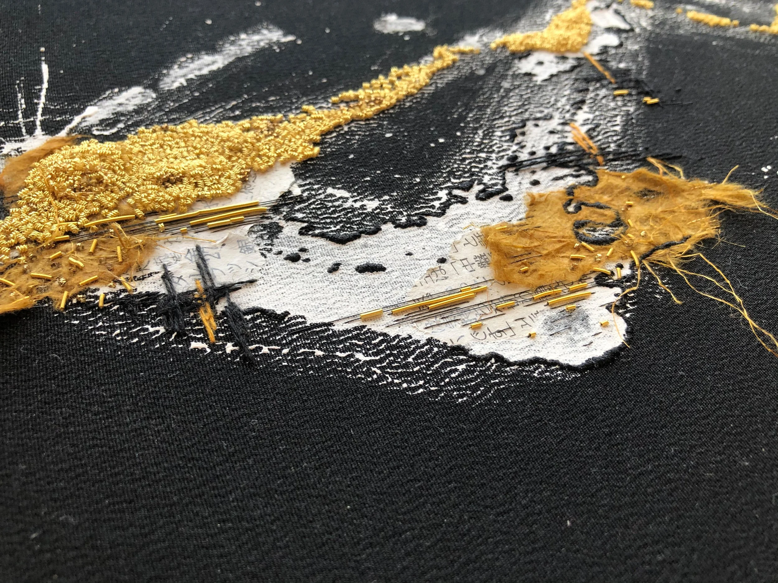 Close-up of textured abstract art with gold and black elements, beads, and fibers on a canvas.