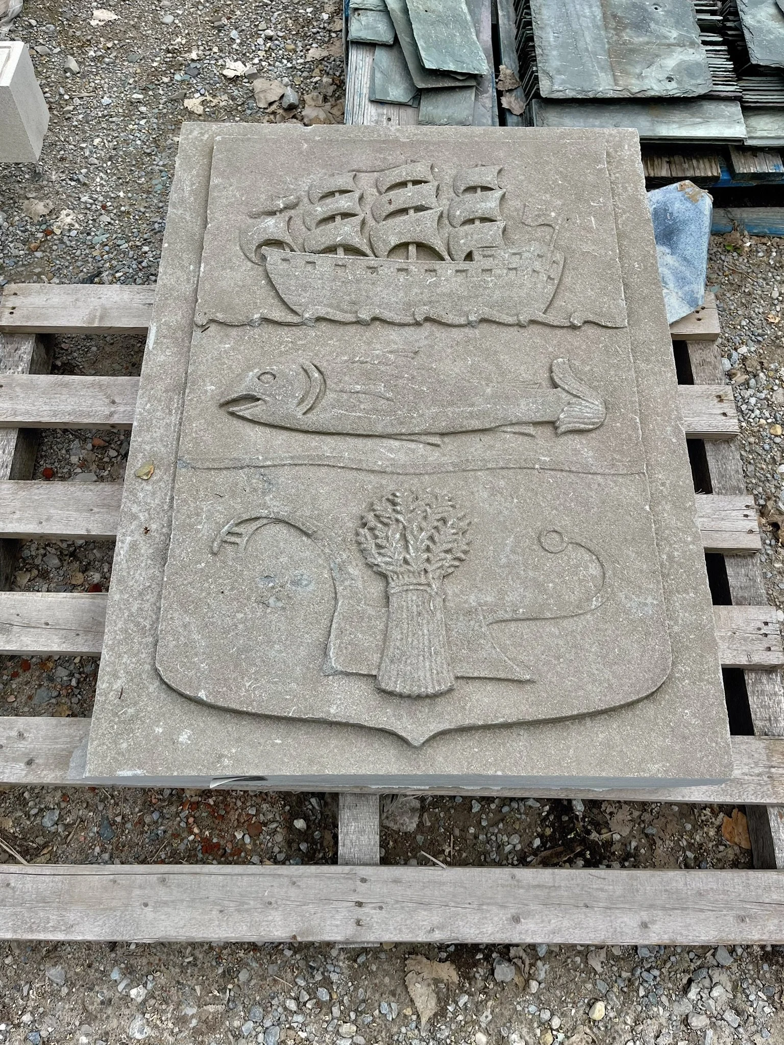 Reclaimed stone panel accent from a historic building with carvings of a ship, fish, and wheat sheaf