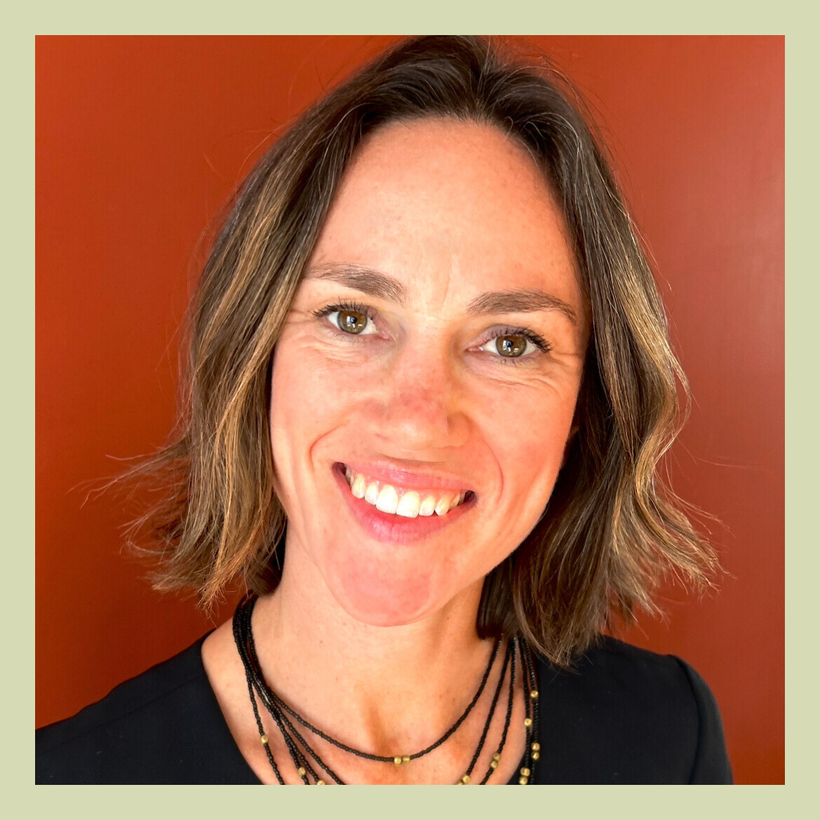 Dr. Alison Lee, DO smiling with short hair against a red background, wearing a black shirt and beaded necklace.