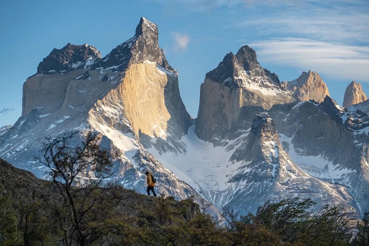 una persona caminando en un paisaje montañoso con picos nevados y un cielo azul