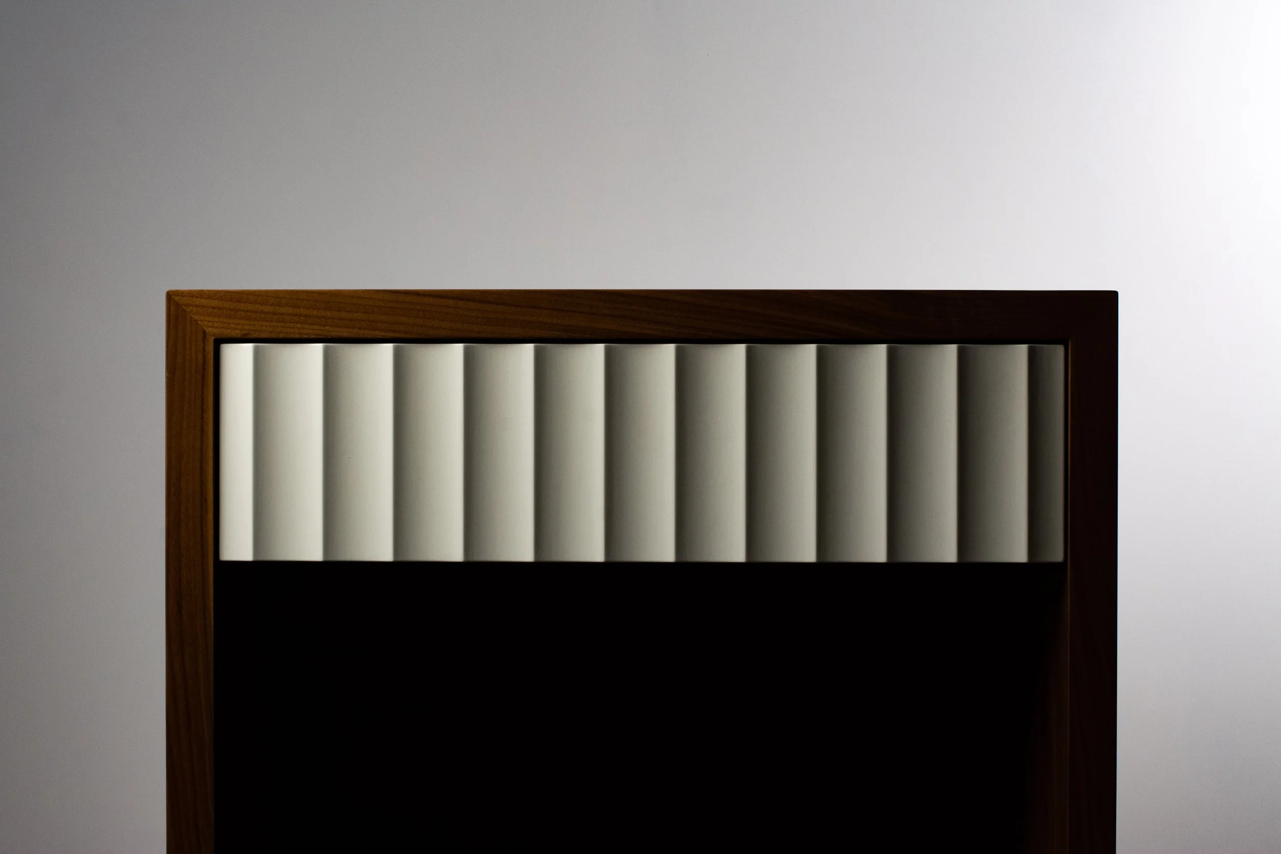 A close-up of a wooden-framed object with vertical white bars against a plain neutral background.