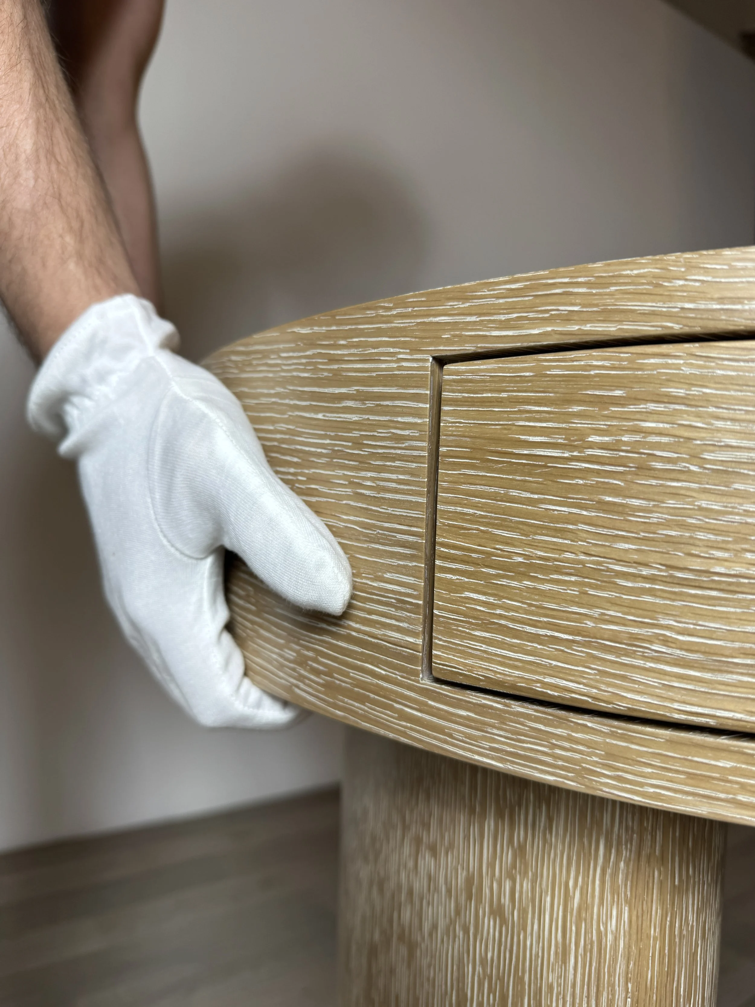 A person wearing a white glove holding a wooden drawer that is pulled out partially, revealing the interior of the drawer with a wood grain pattern.