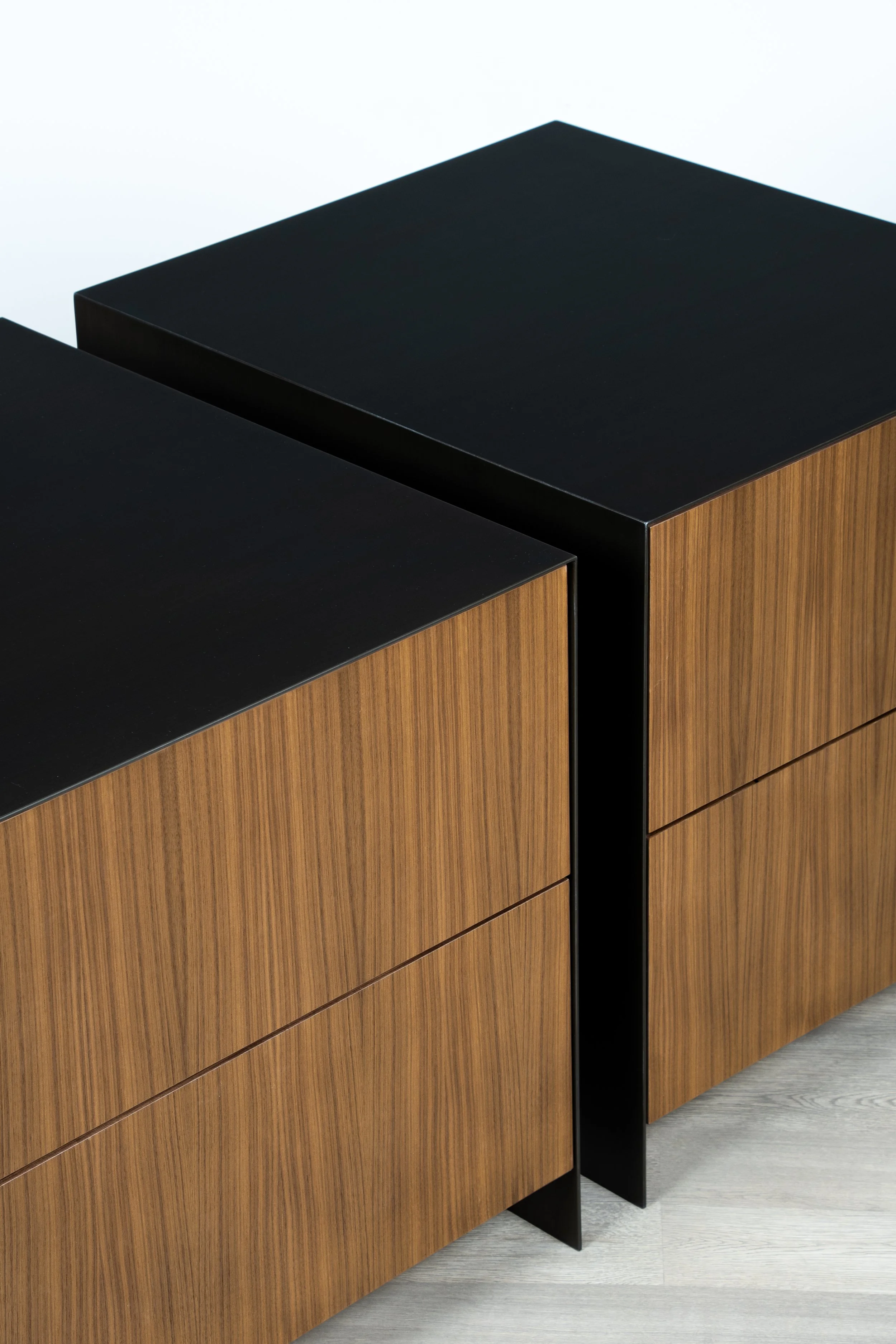 Close-up of a modern wooden cabinet with black metal handles and trim, placed on a light-colored wood floor.